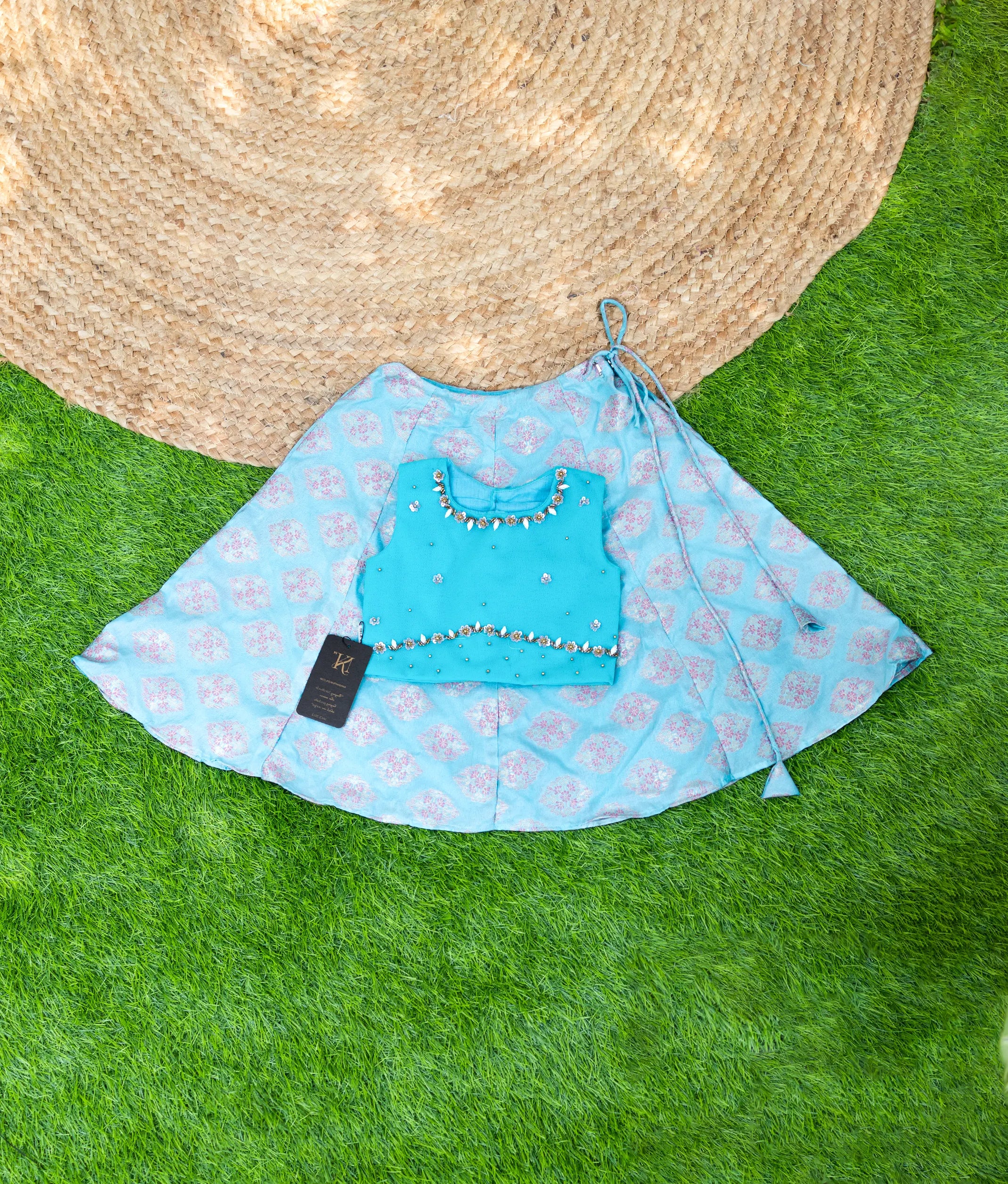 Sky blue handwork top with peach skirt laid out on a green surface, traditional wear.
