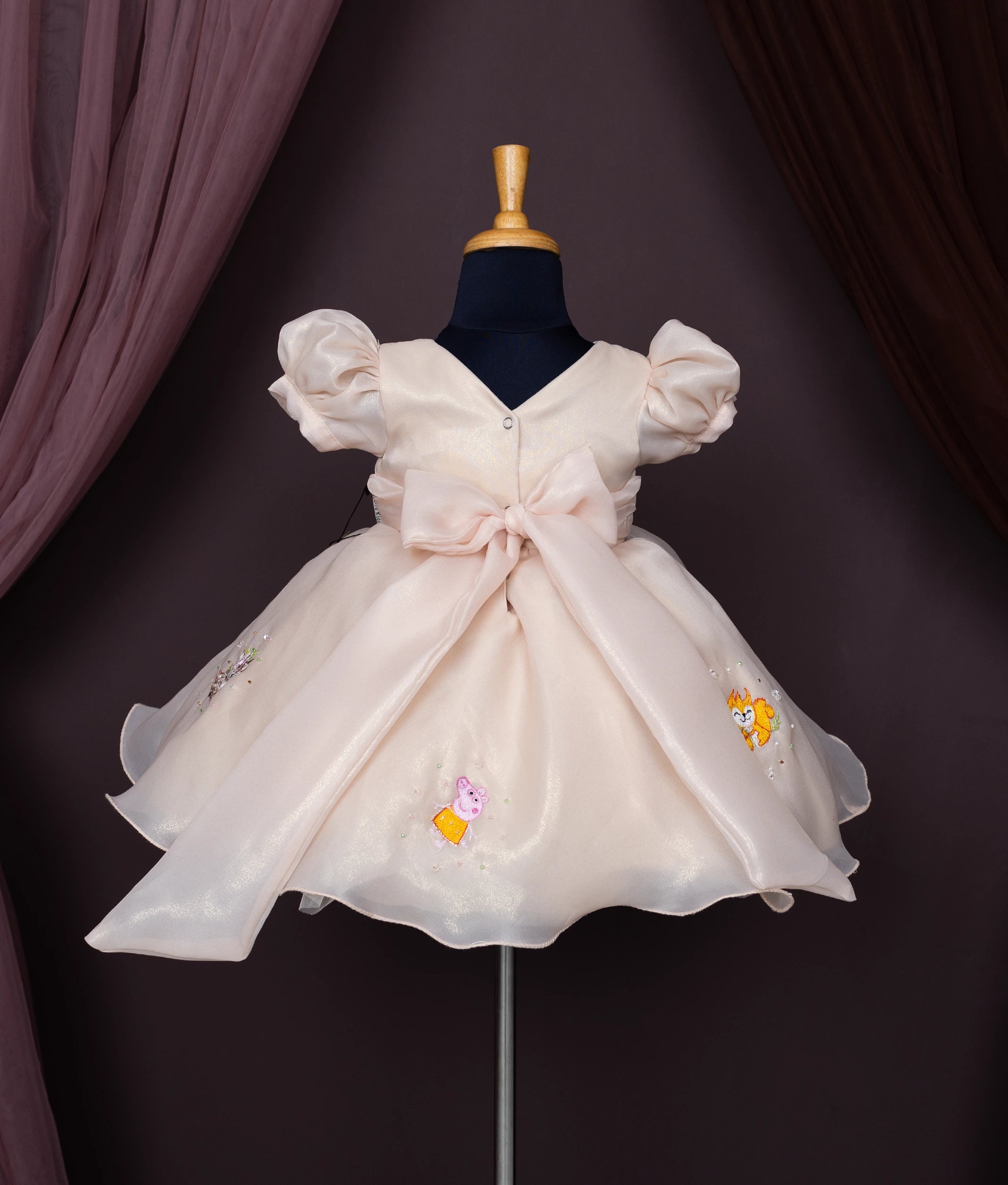 Back view of a beige baby girl dress with puff sleeves, a Peter Pan collar, and cartoon forest animal embroidery.