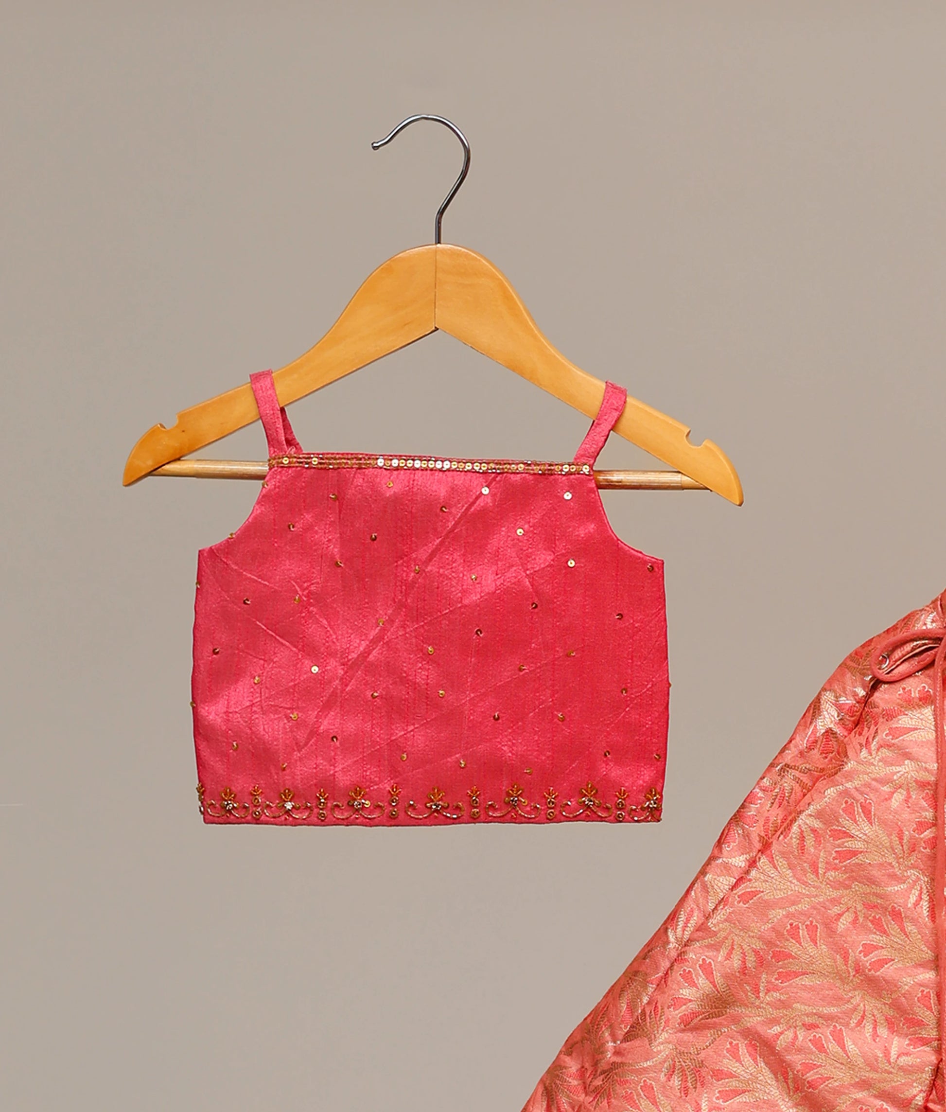Close view of kids' hot-pink lehenga choli set with a handwork-embellished top and a floral banarasi skirt.