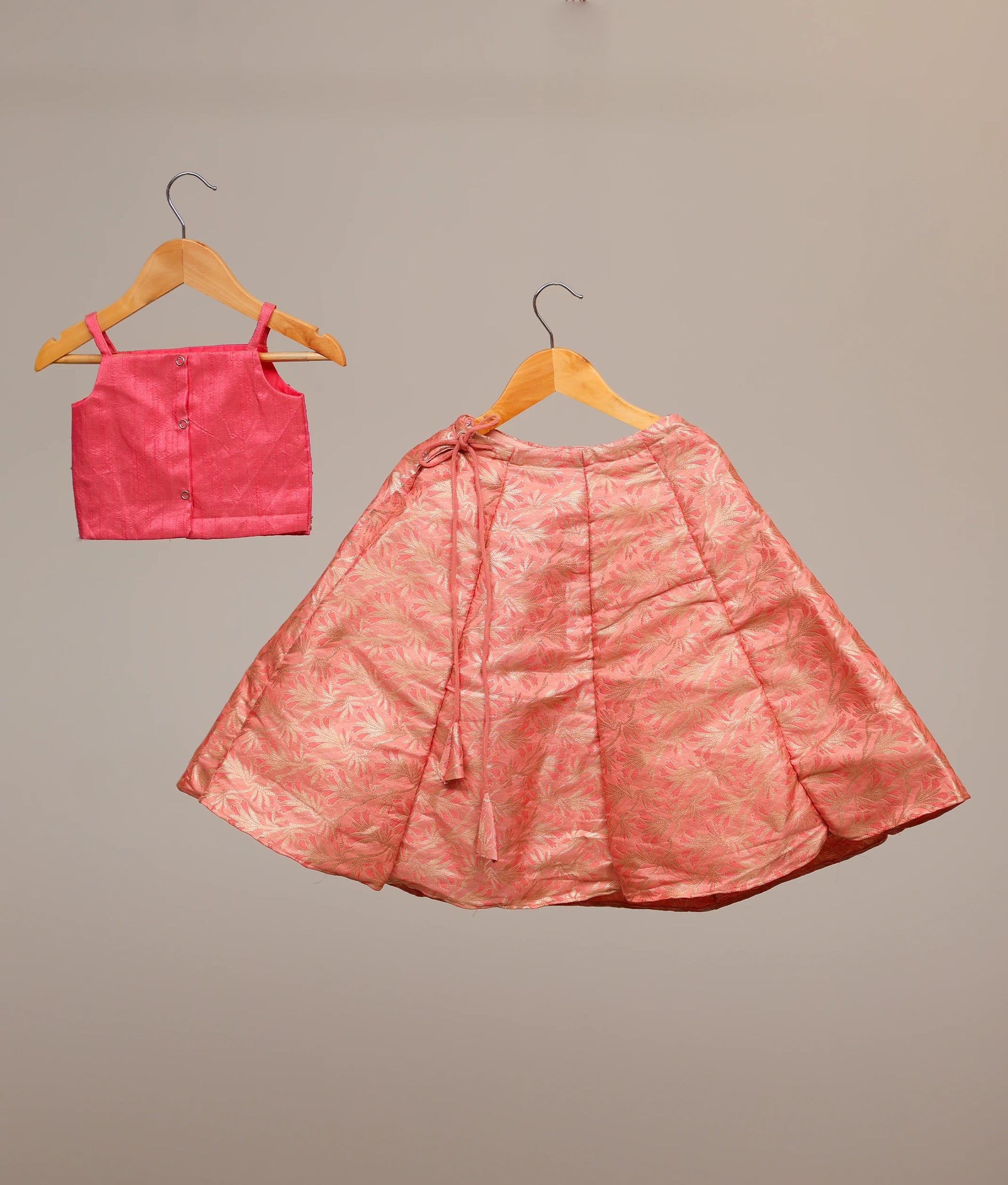 Back view of kids' hot-pink lehenga choli set with a handwork-embellished top and a floral banarasi skirt.