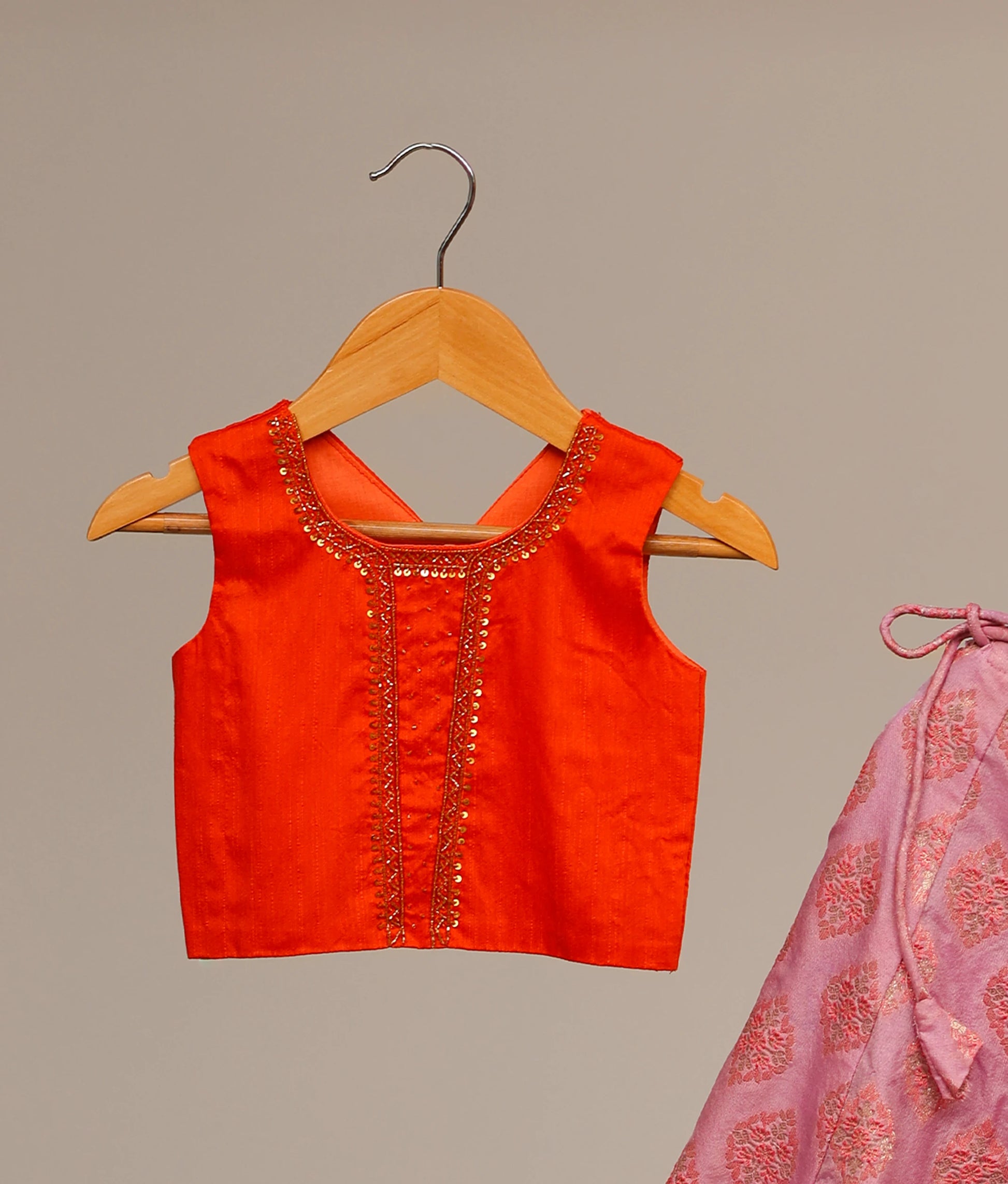 Close view of an orange raw cotta embellished crop top and a lilac banarasi printed skirt, a traditional Indian lehenga choli for kids.