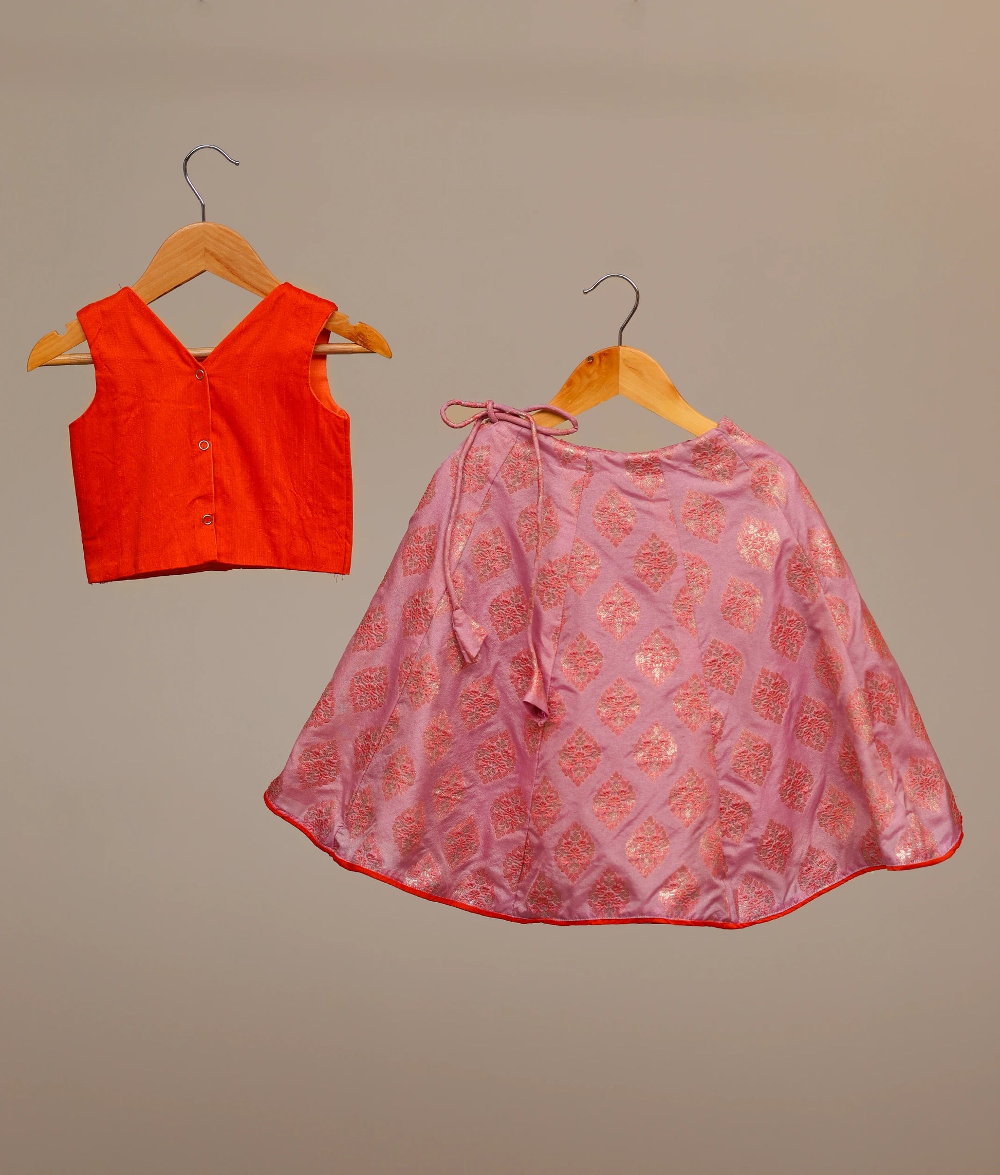 Back view of an orange raw cotta embellished crop top and a lilac banarasi printed skirt, a traditional Indian lehenga choli for kids.