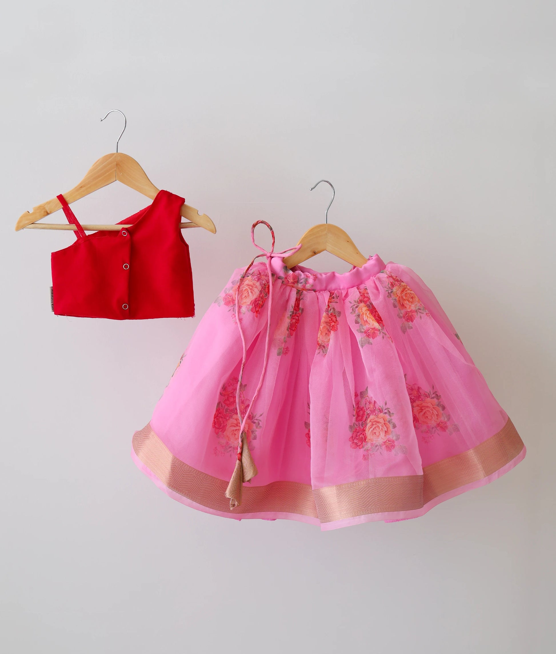 Back view of a red and pink kids' lehenga set. One-shoulder top with handwork. Pink skirt with floral prints