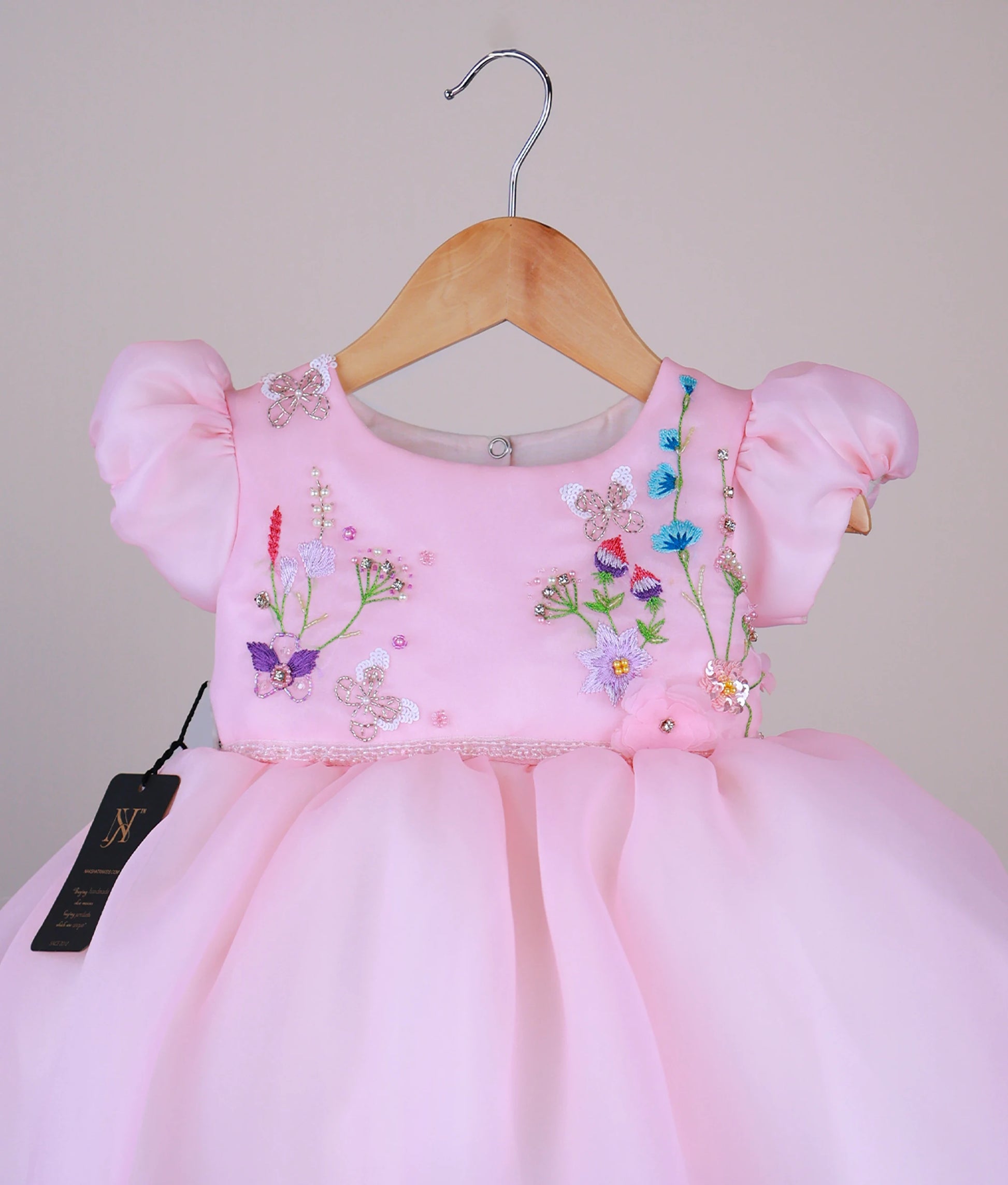 Close view of a plain pink organza baby girl frock with embroidered butterfly and floral designs on the bodice