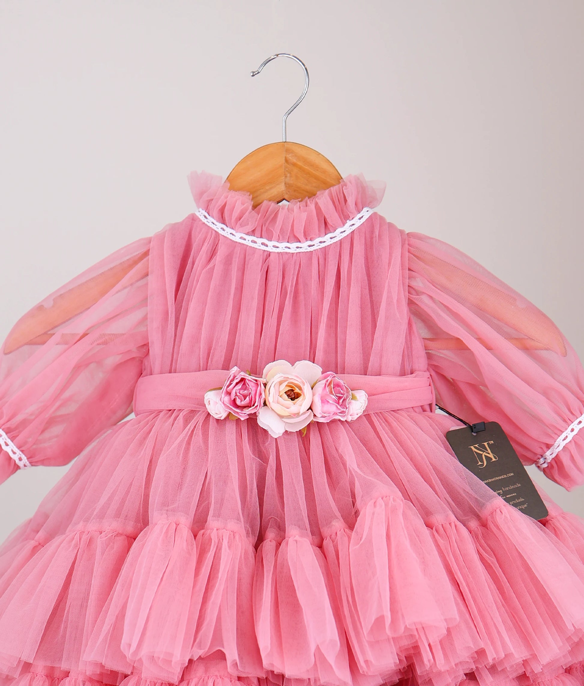 Close view front View of an onion-pink tulle net birthday frock hanging on a white background.