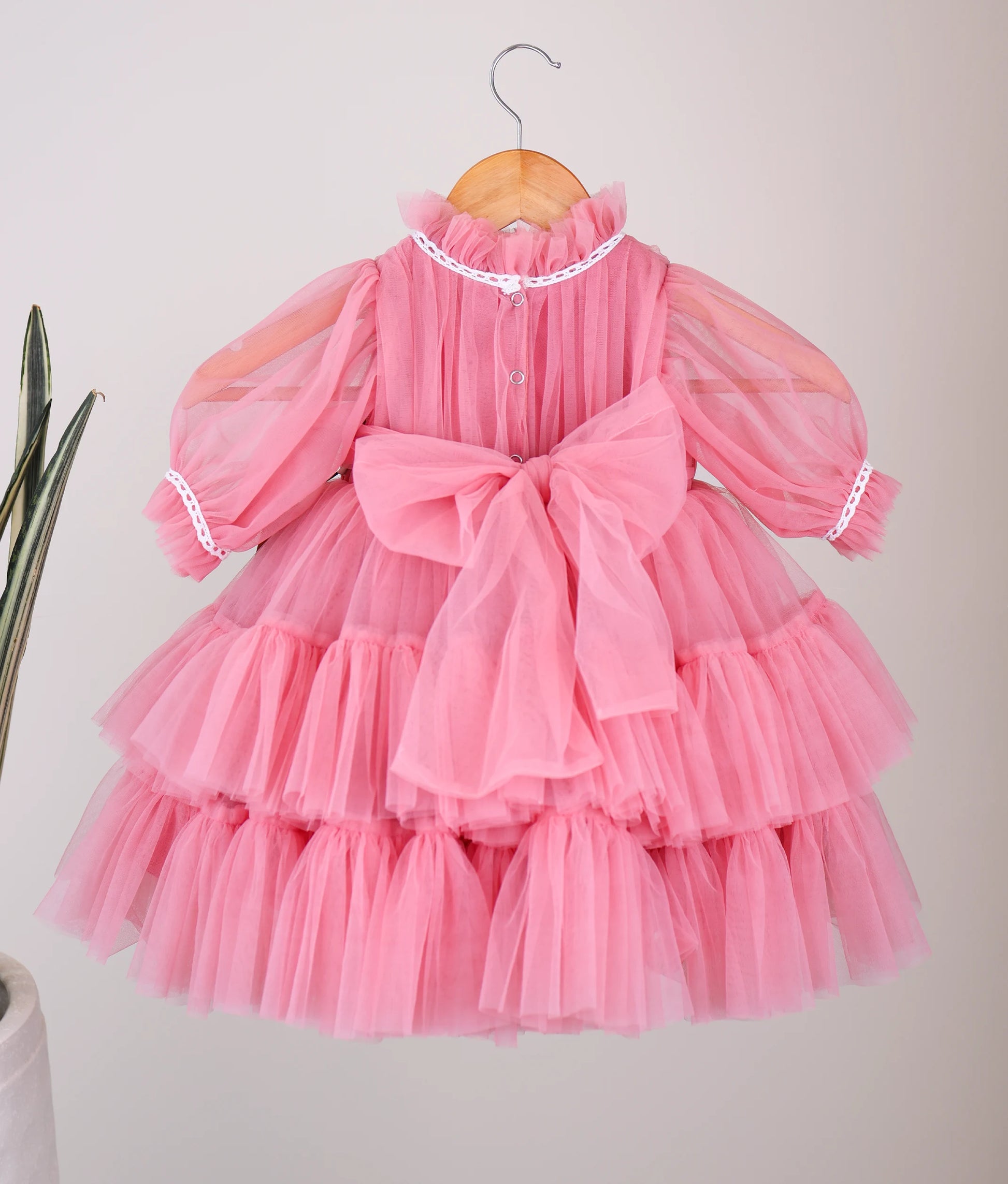 Back  View of an onion-pink tulle net birthday frock hanging on a white background.