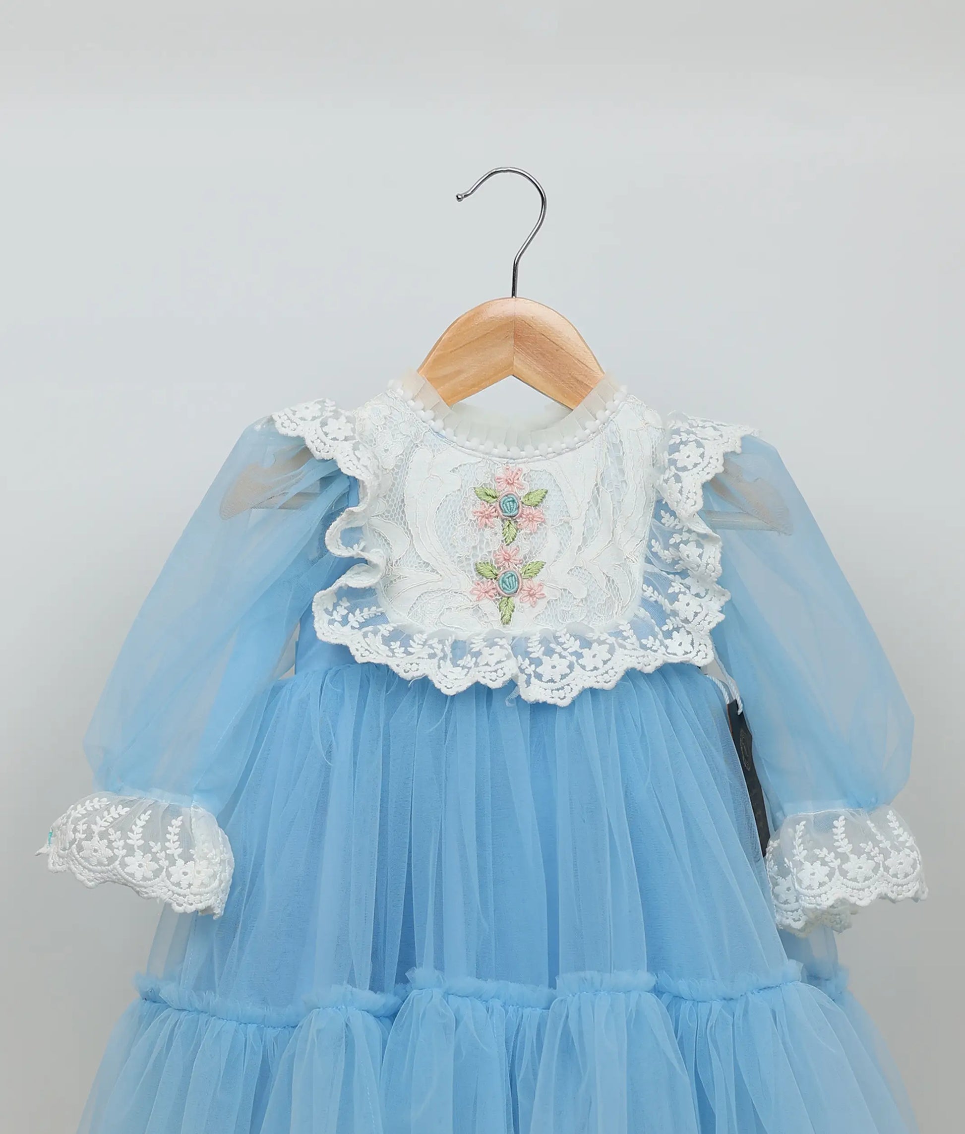 Close view of blue floral embroidery and lace birthday frock against plain background 