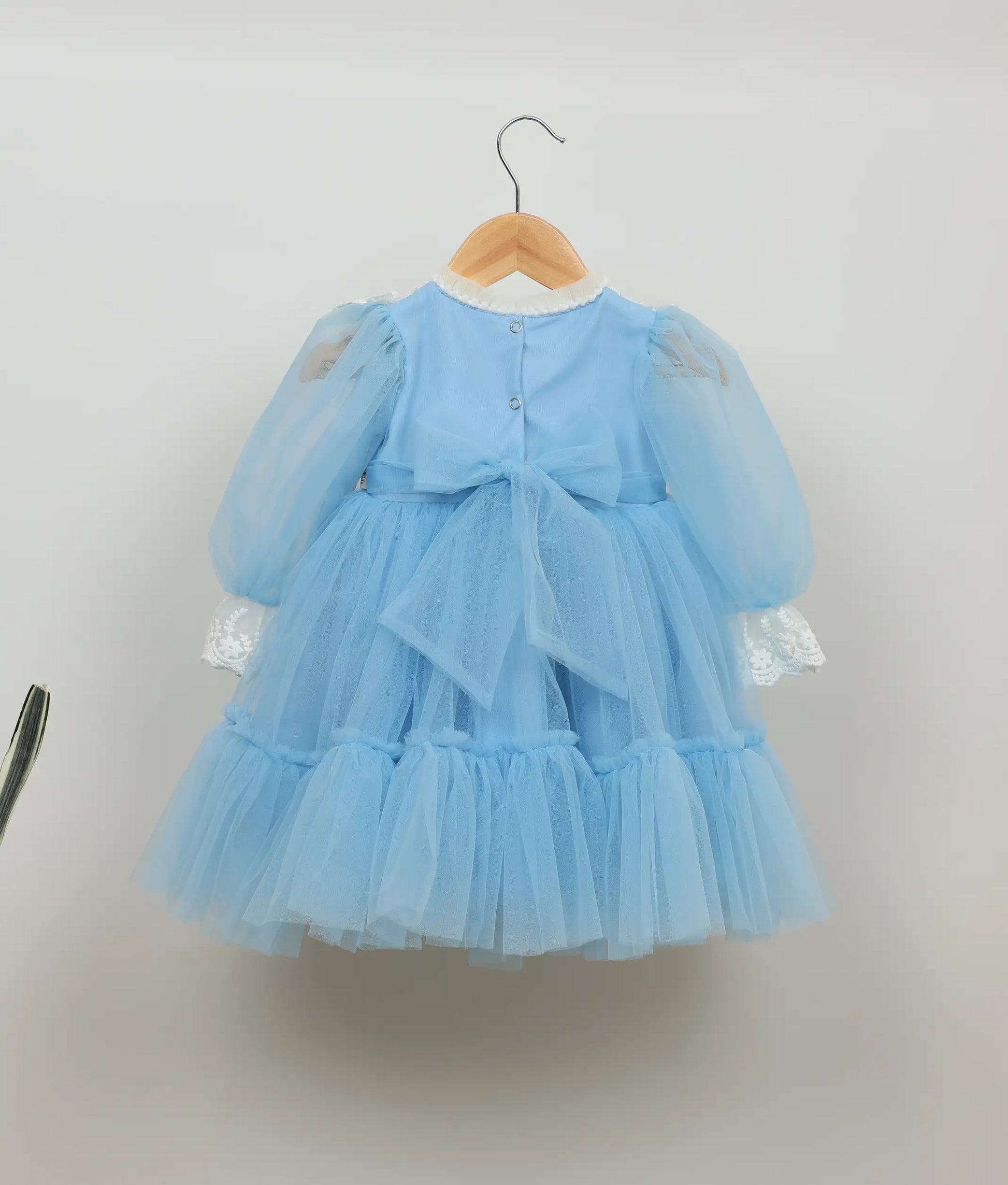 Back view of blue floral embroidery and lace birthday frock against plain background 