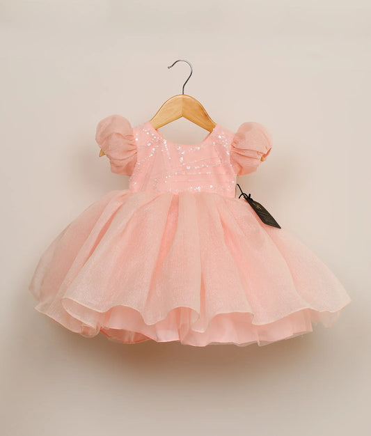 Front view of a pastel pink crush organza birthday frock against plain background