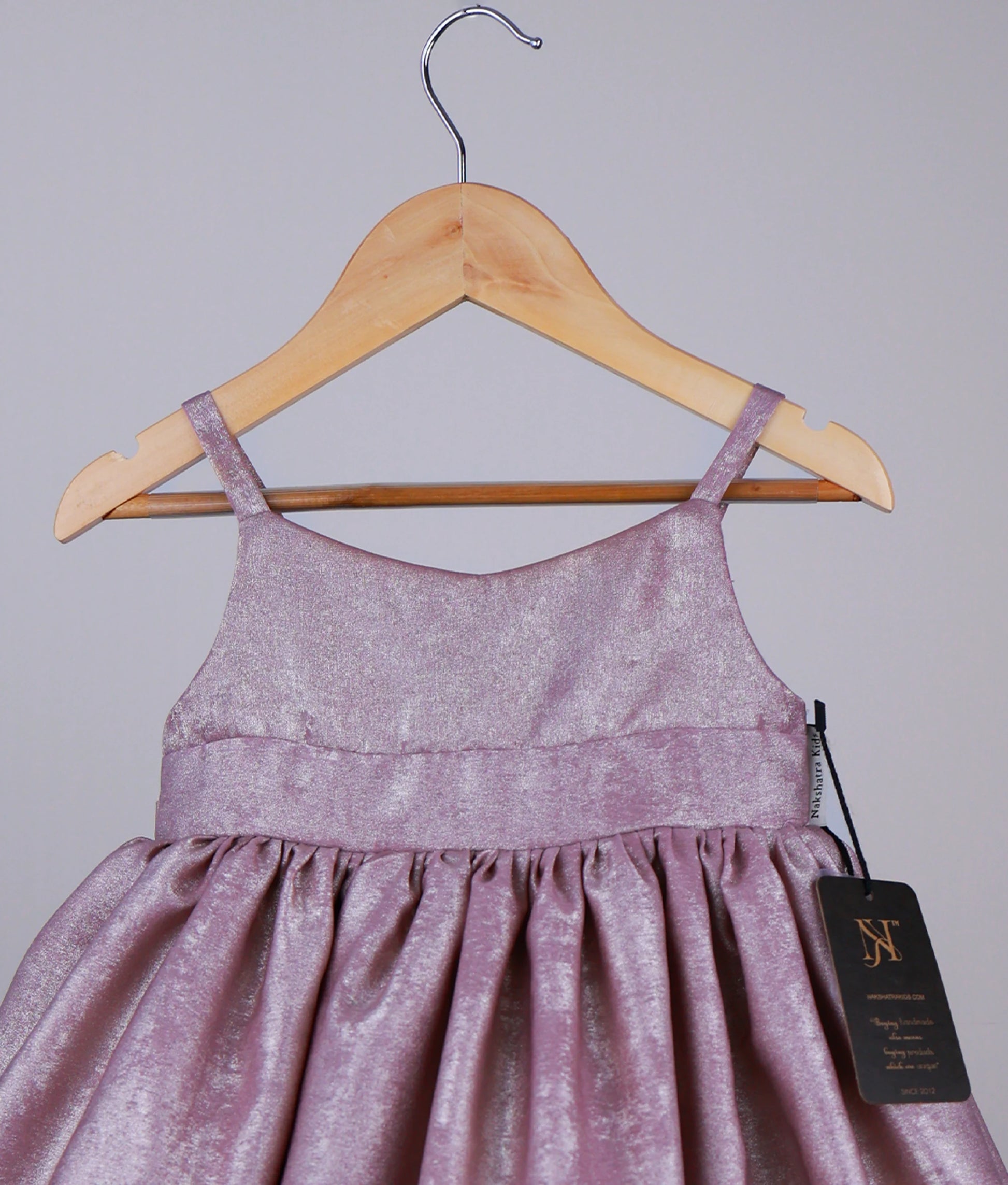 Close view of an onion pink gown on a hanger with a visible tag against a plain background.