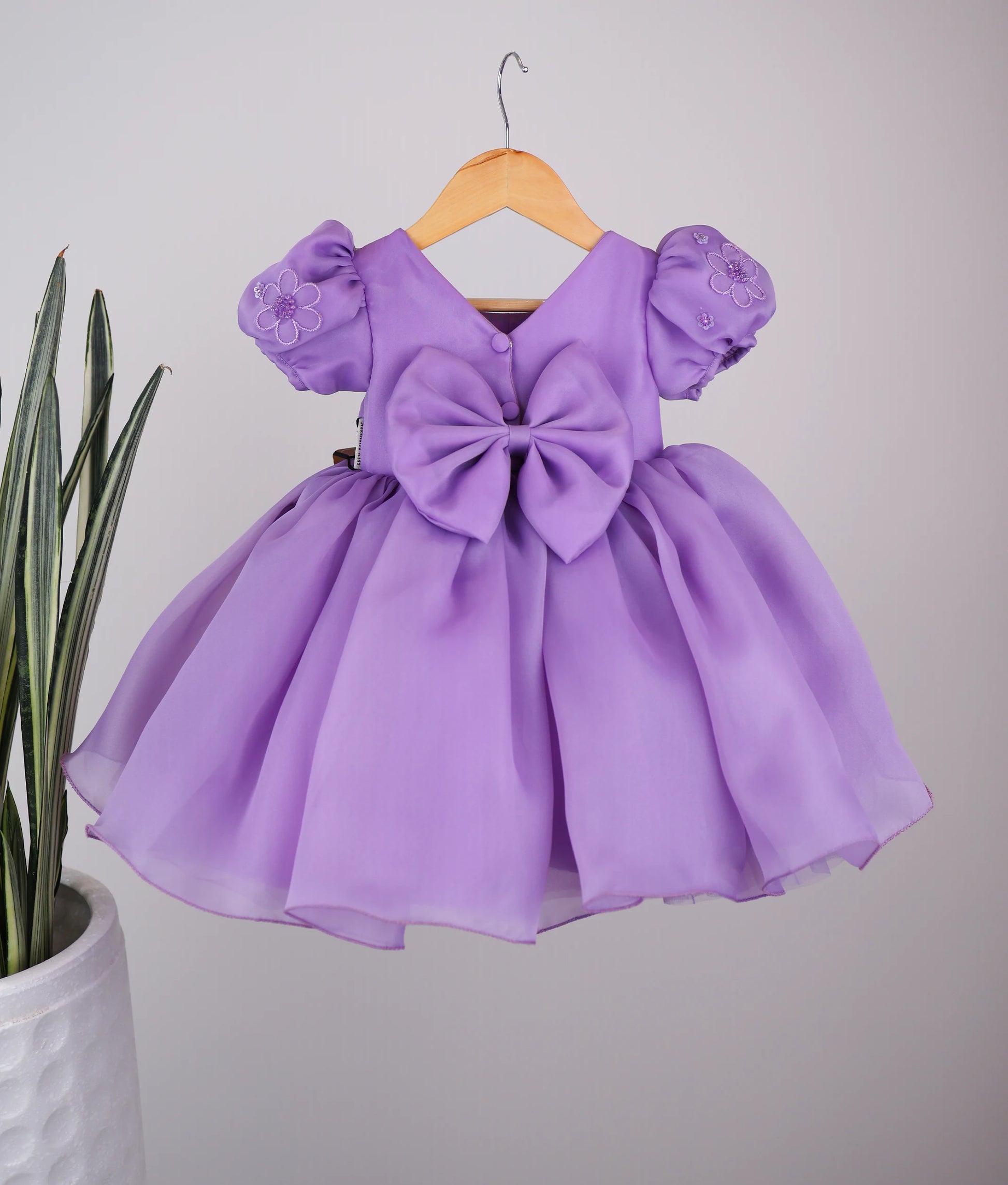 Back view of handworked flower-themed baby girl dress against white background