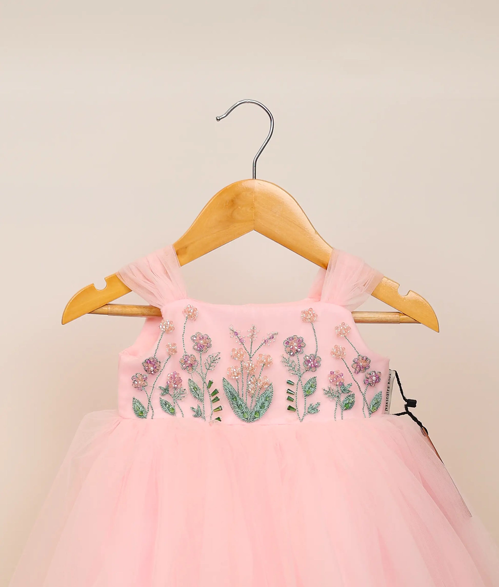 Close view of pink tulle net floral handworked birthday frock against plain background