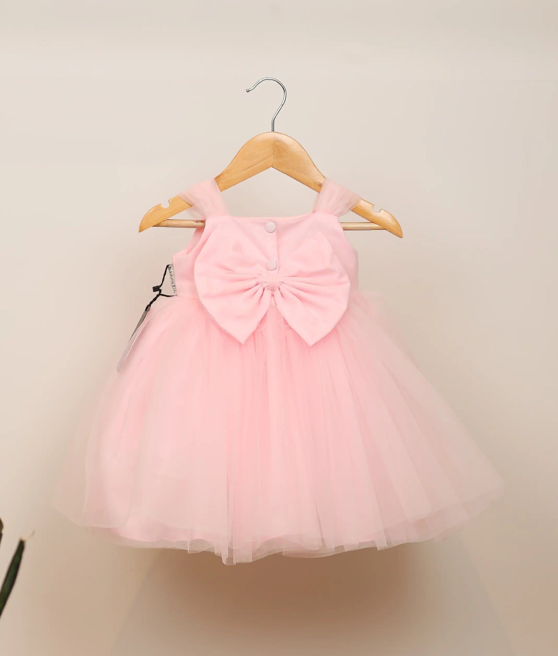 Back view of pink tulle net floral handworked birthday frock against plain background