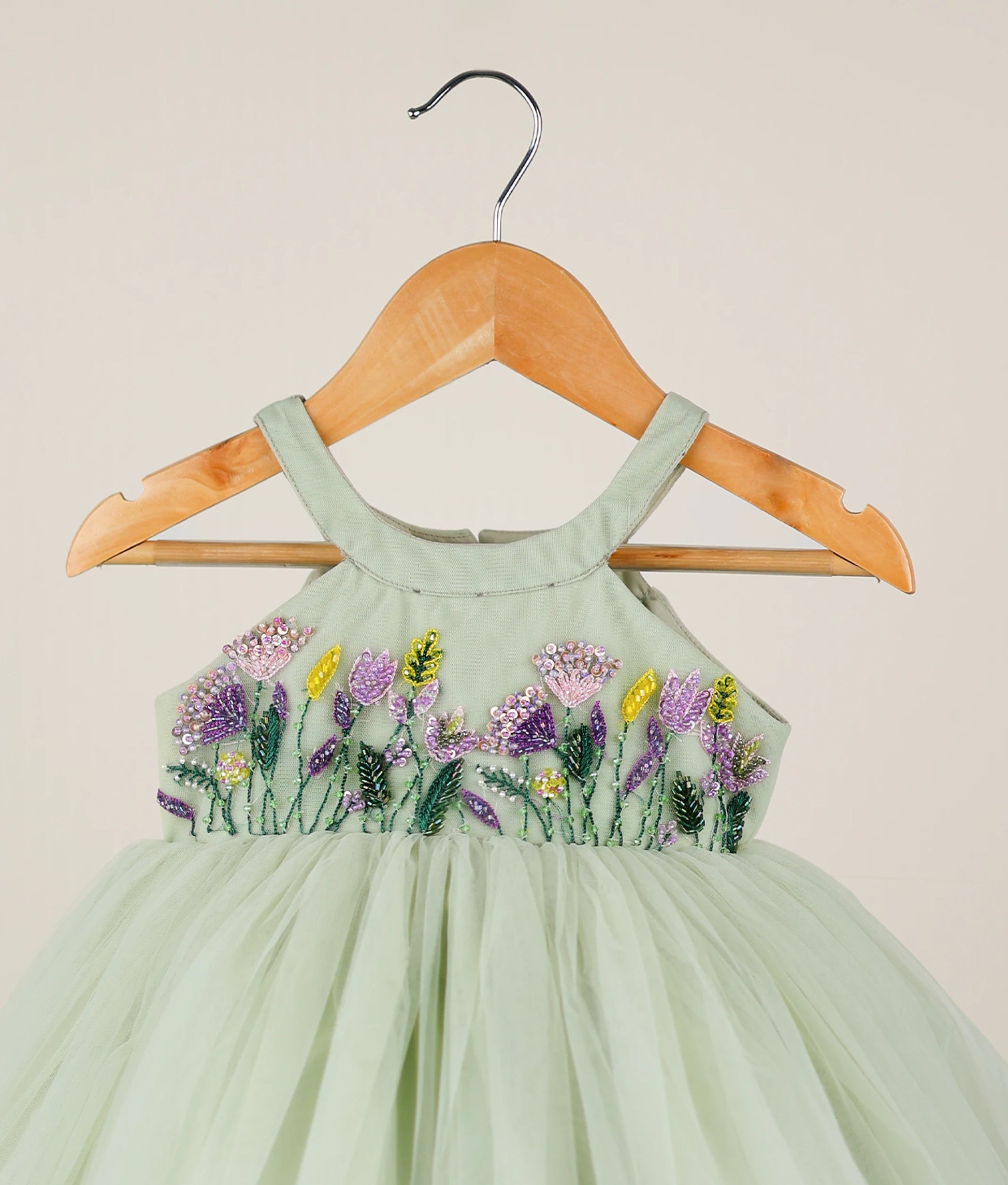 Close view of pastel green tulle net floral handworked birthday frock against plain background 
