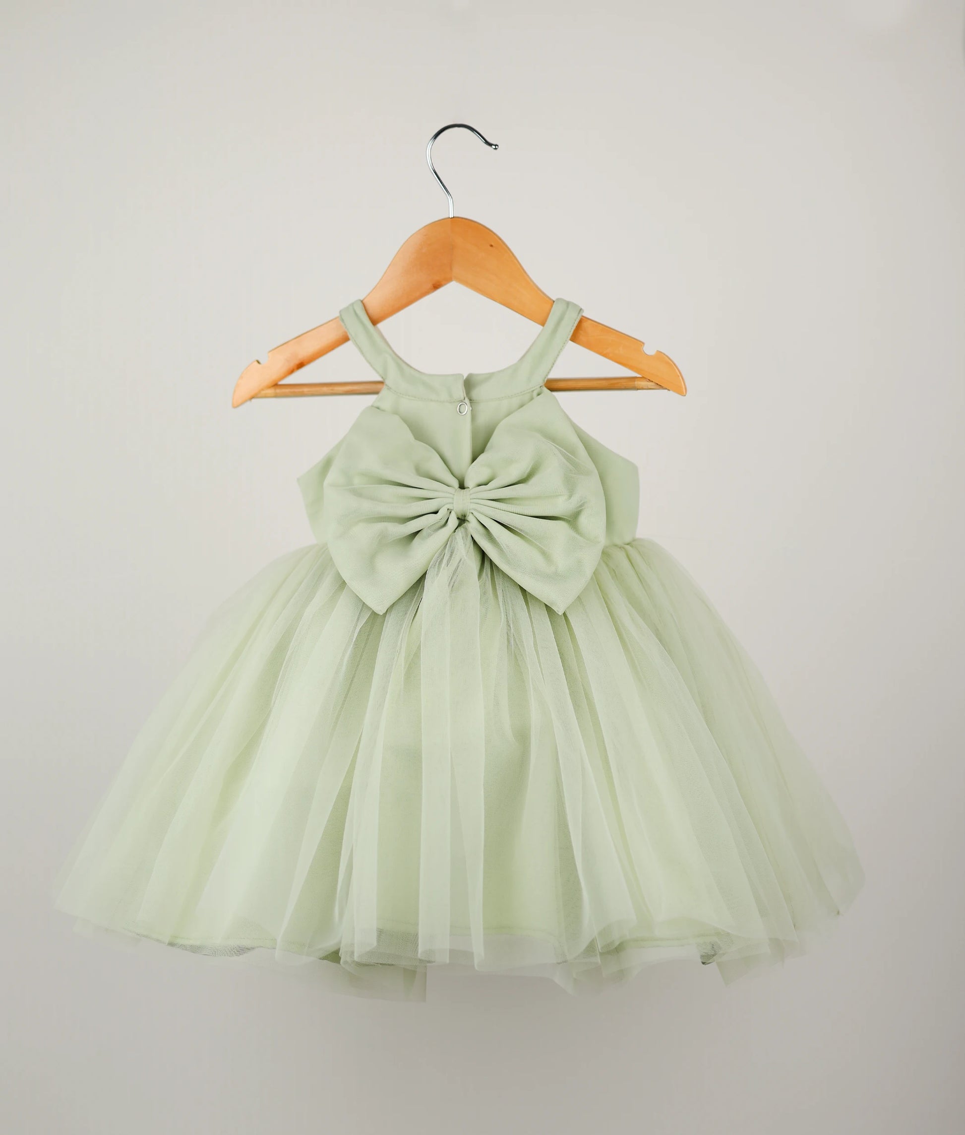 Back view of pastel green tulle net floral handworked birthday frock against plain background 