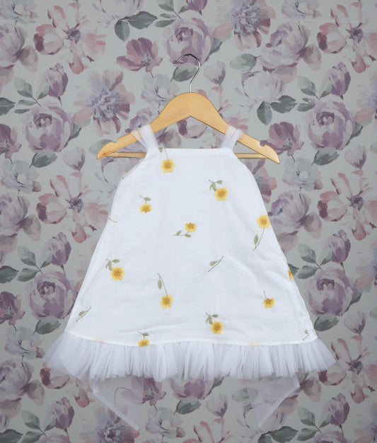 White dress with yellow floral patterns on a hanger against a floral wallpaper background.