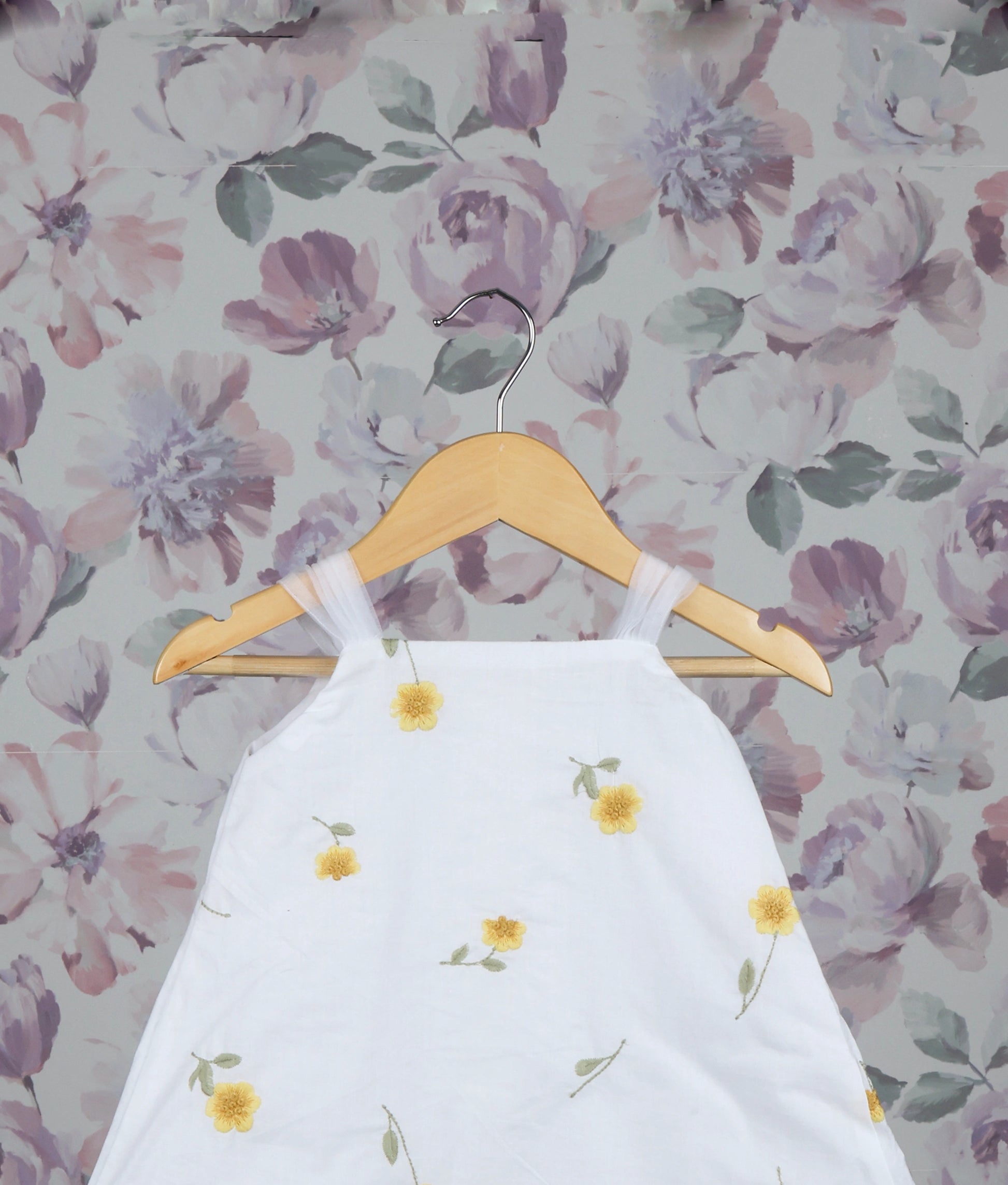 Close view of a White dress with yellow floral patterns against a floral wallpaper background.