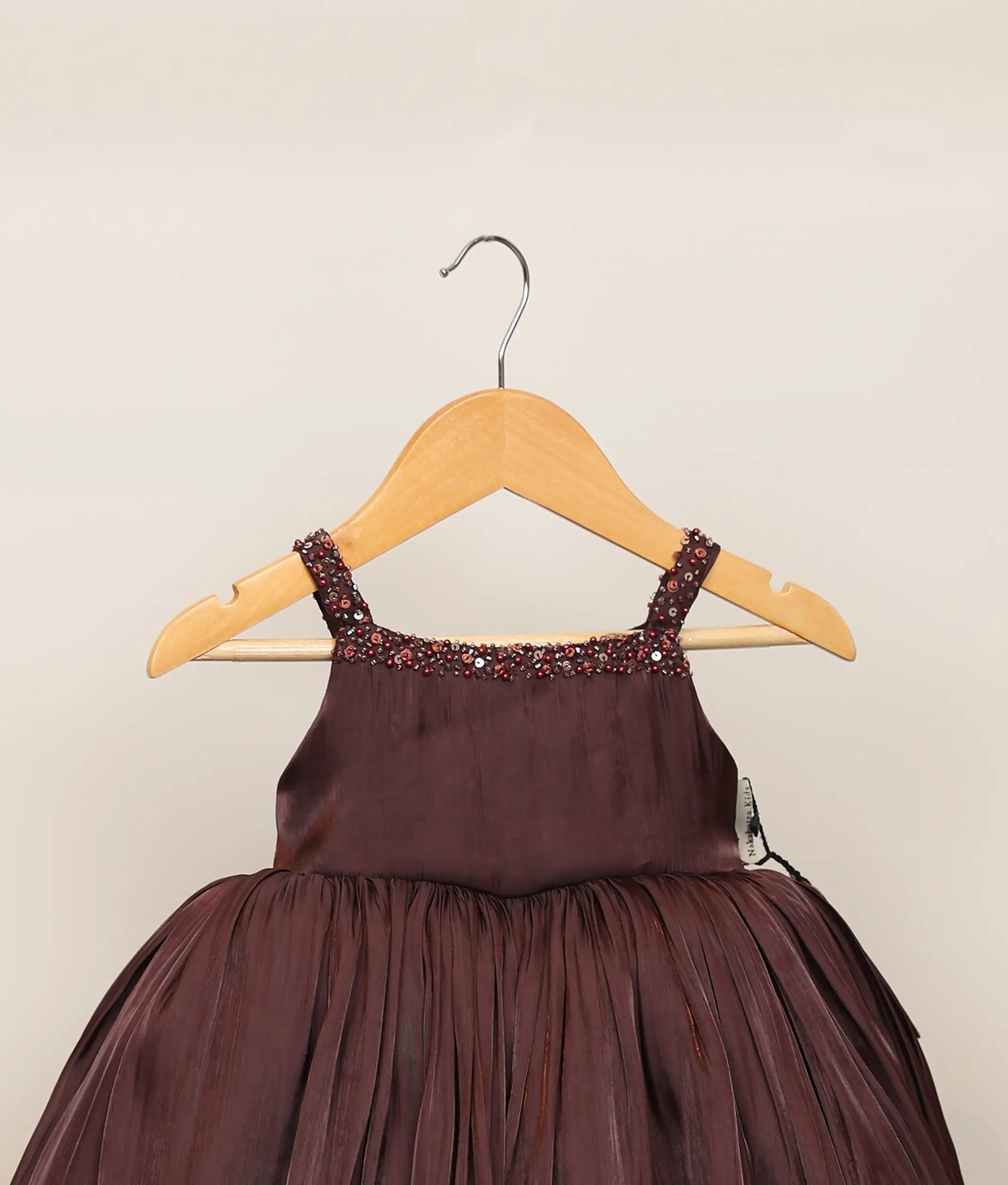 Close view of a coffee-brown lacer organza handworked birthday frock against plain background