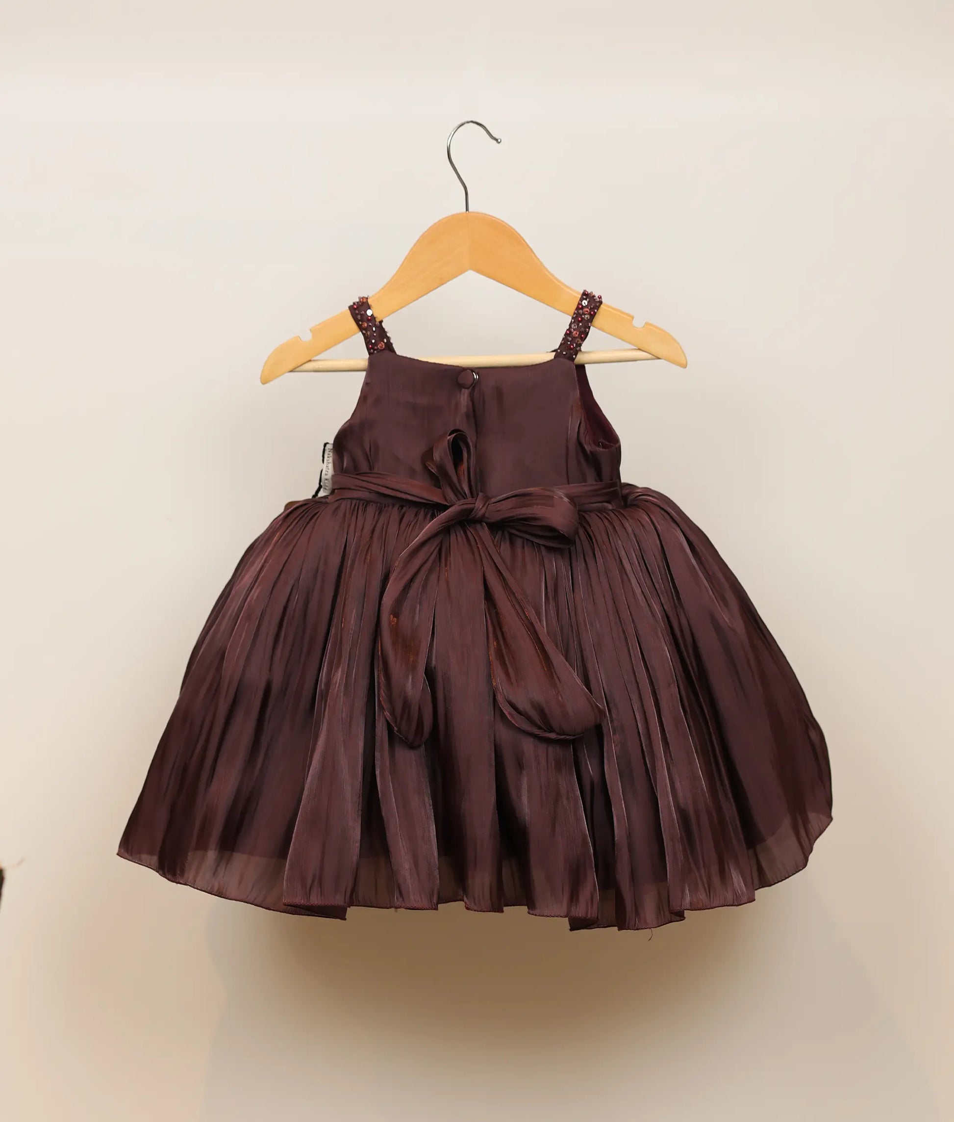 Back view of a coffee-brown lacer organza handworked birthday frock against plain background