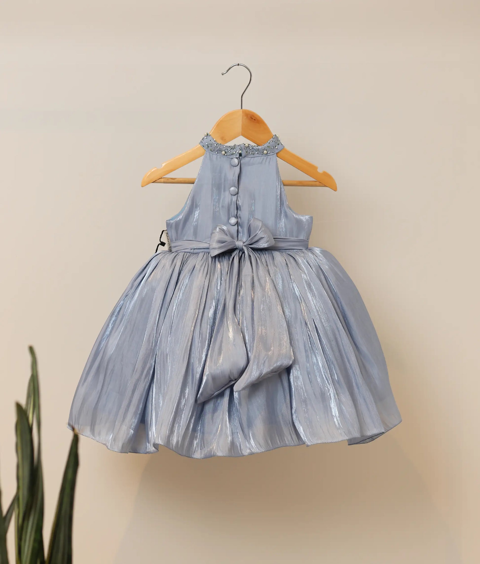 Back view of ash blue laser organza floral, handworked birthday frock against plain background