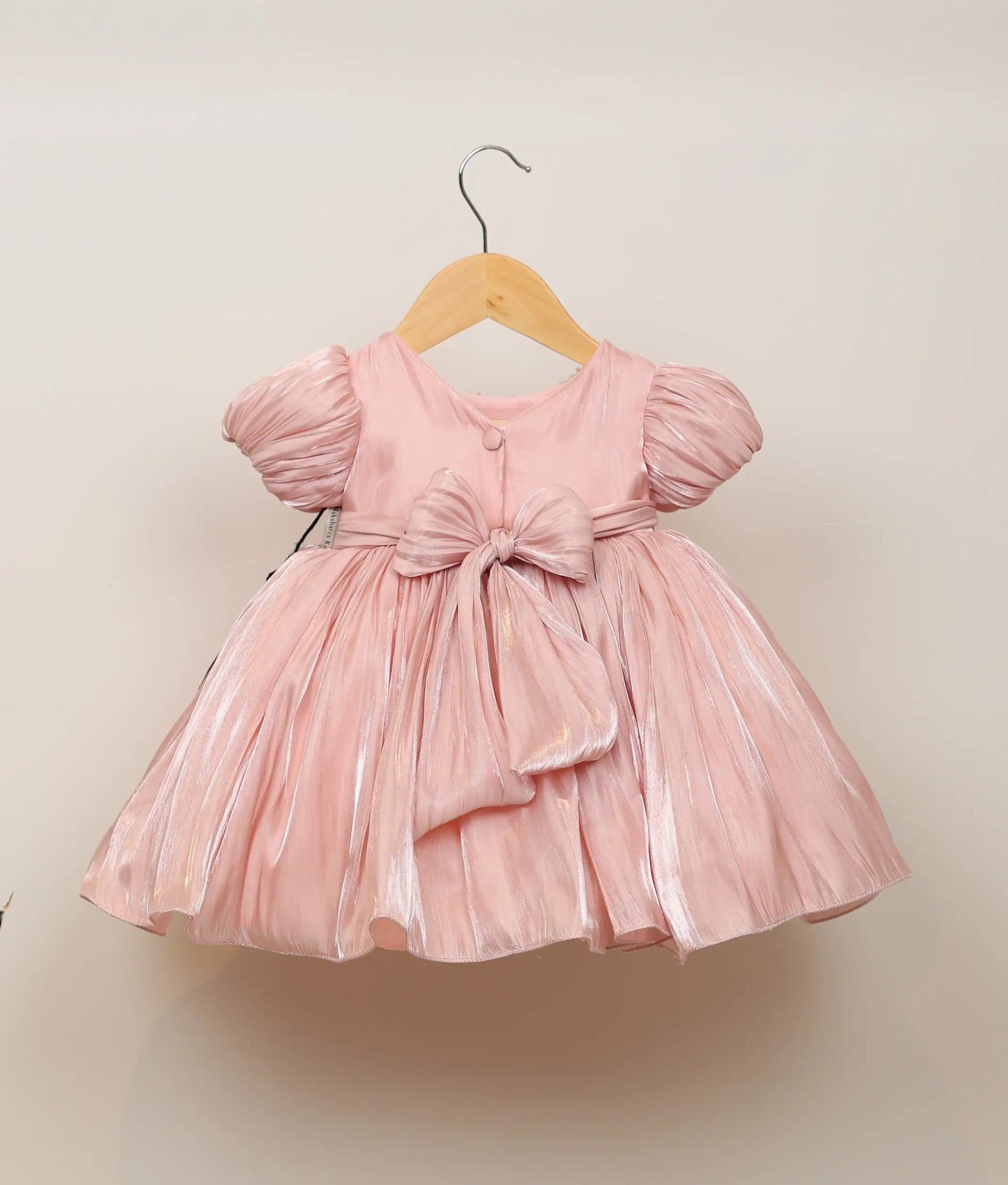 Back view of a peach lacer organza floral hand-worked birthday frock against plain background 