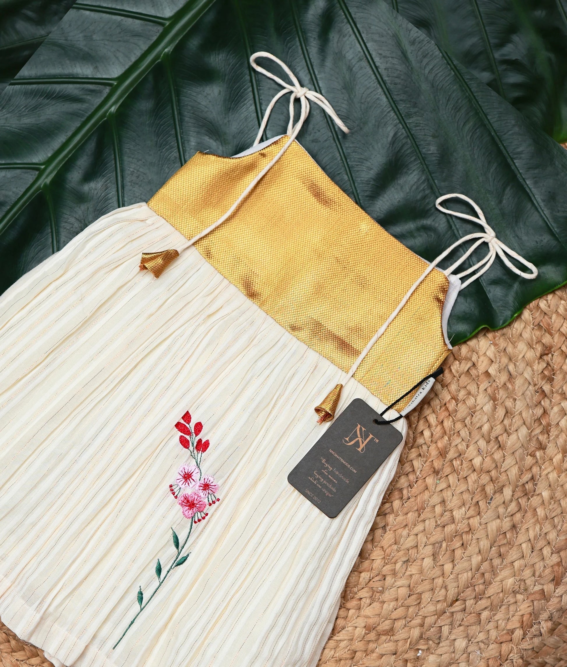 Close view of a golden and off-white frock on a leaf and woven mat background.