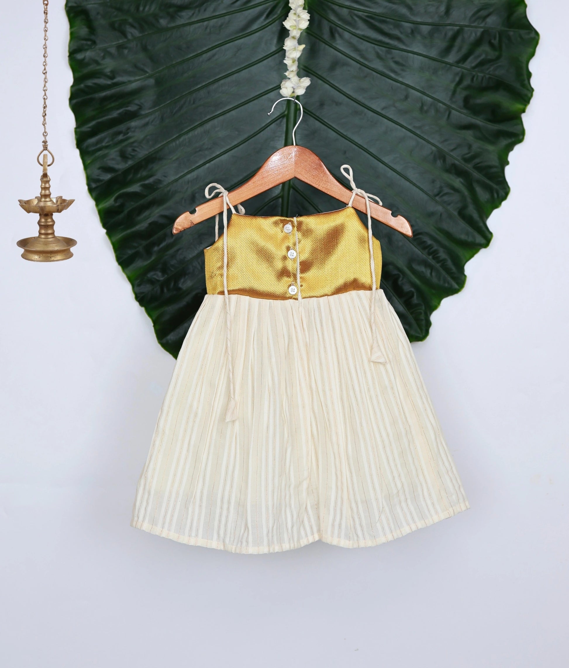 Back view of a golden and off-white frock on a hanger with a leafy background.