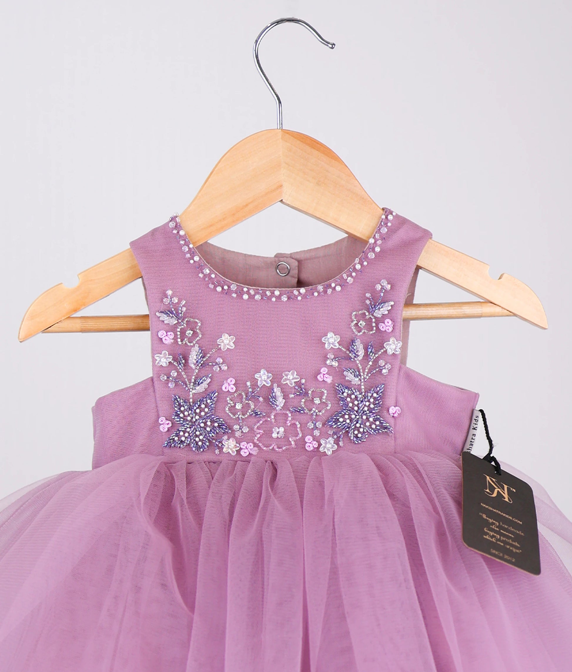 Close view of pastel lavender tulle net handworked birthday frock against plain background 