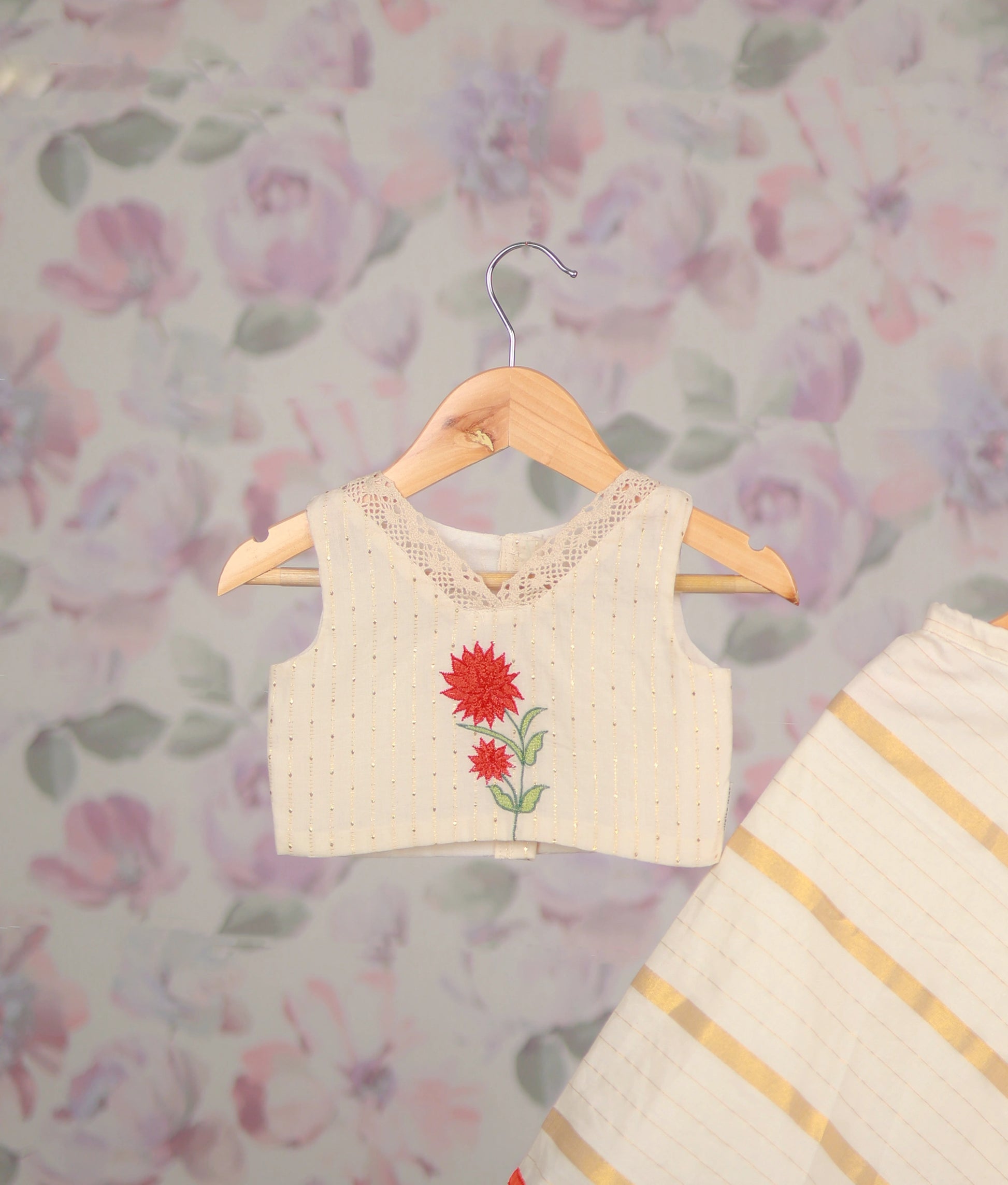 Close view of an off-white floral embroidery top and striped flared skirt with red hemline.