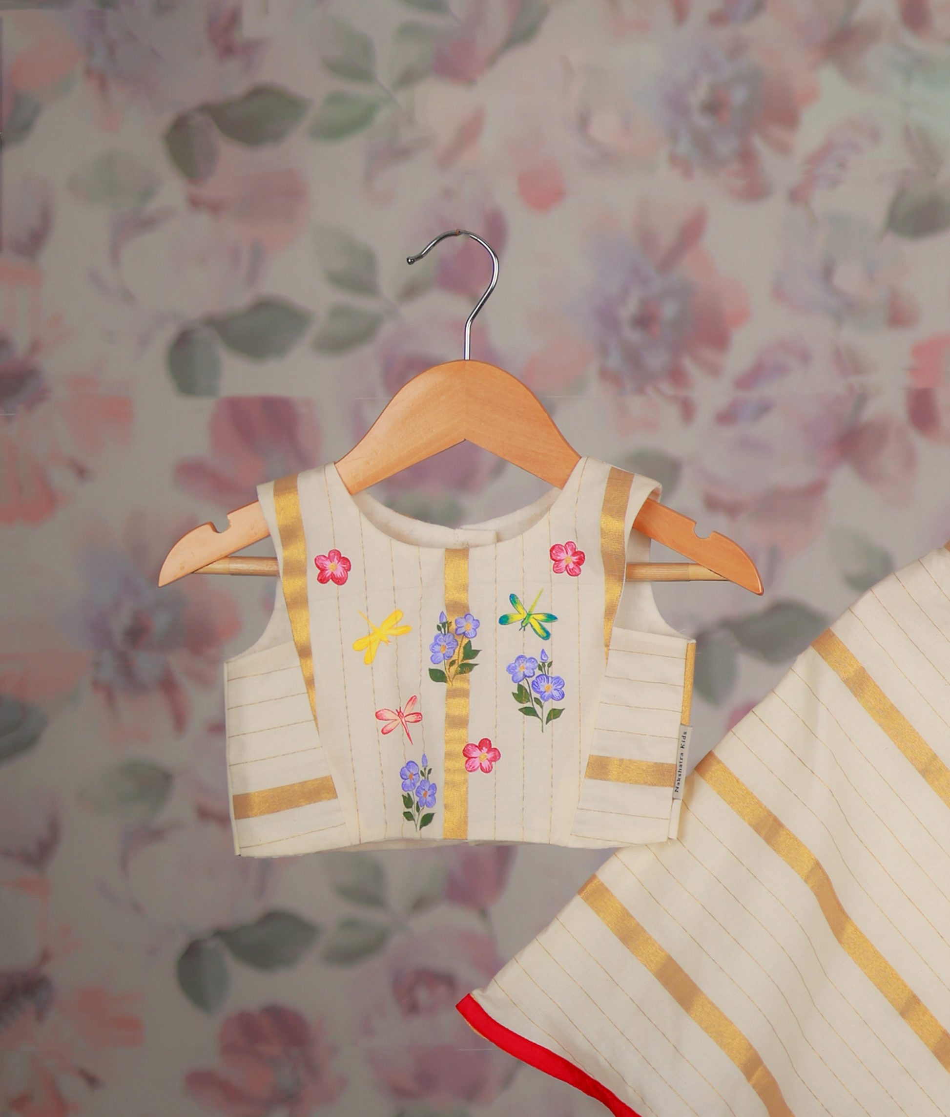 Close view of a floral hand-painted top and a golden striped skirt with a red border hem.