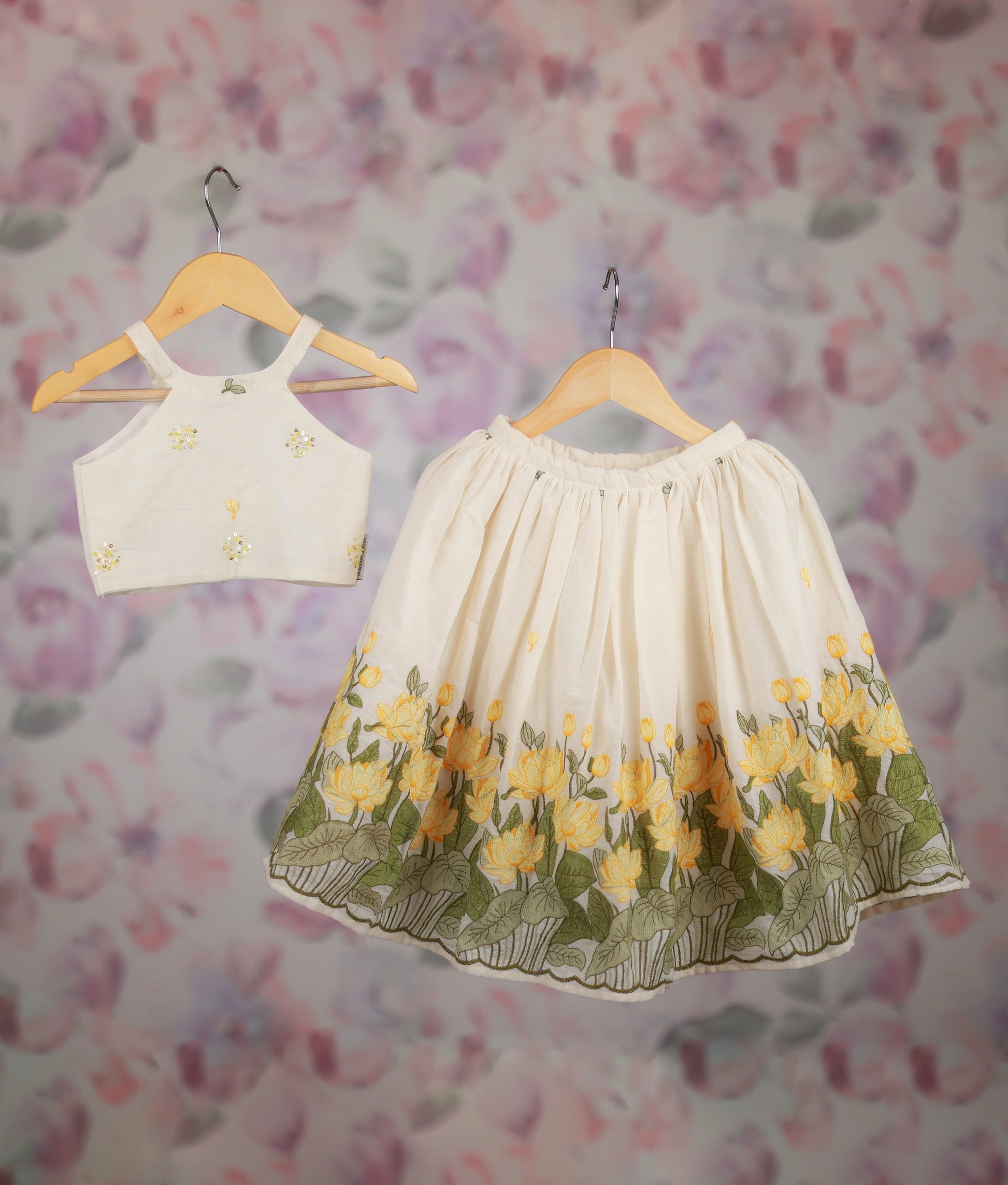 Off-white kids' outfit with a floral embroidered crop top and a yellow lotus border skirt set.