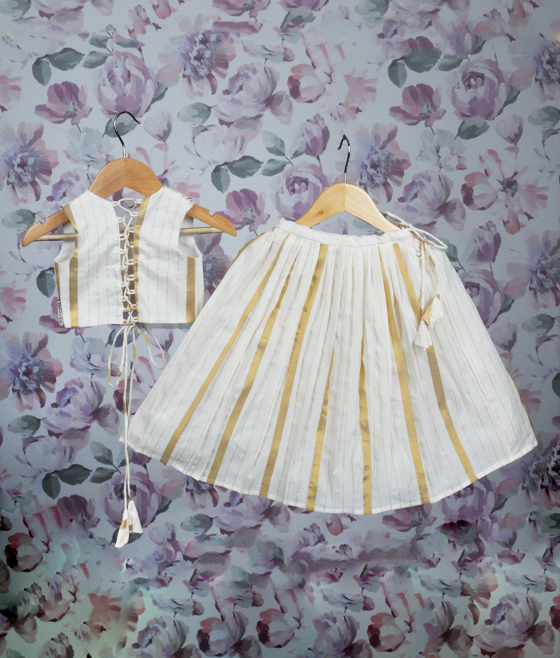 Back view of off-white and gold pleated skirt set with a handworked top on a hanger.