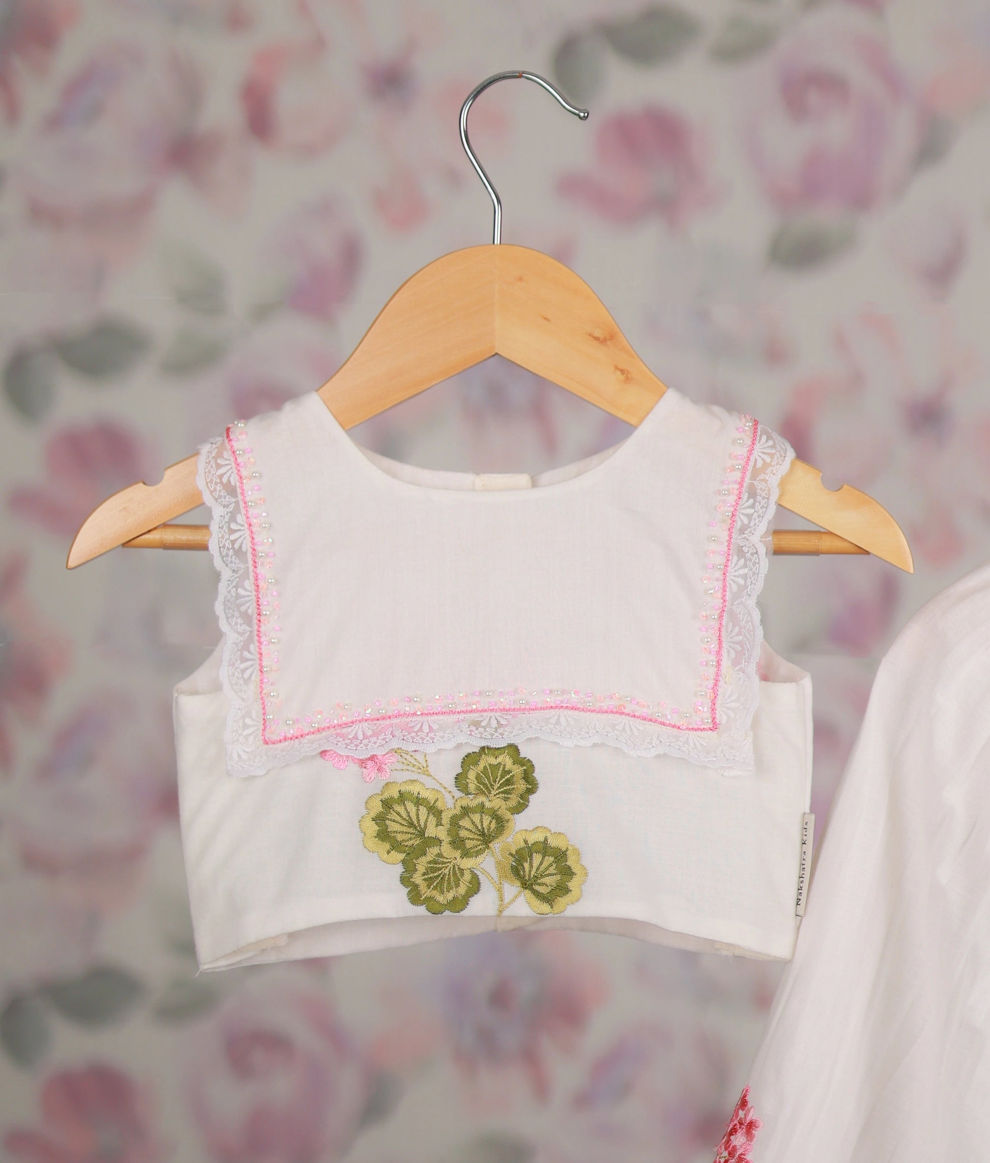Close view of a white top and skirt set with pink floral embroidery and lace trim on wooden hangers.