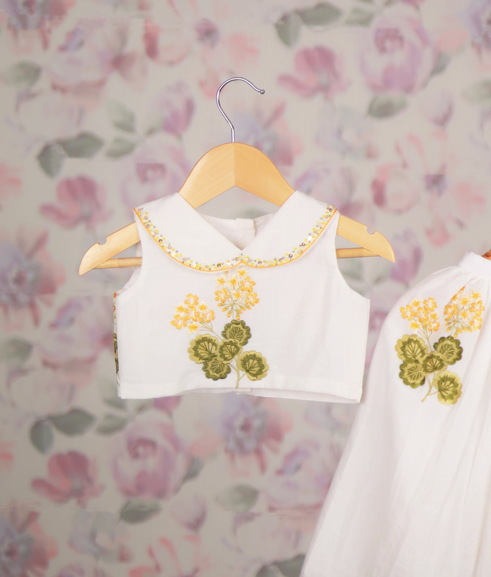 Close view of a white baby girl skirt set with yellow floral embroidery and a Peter Pan collar top, ethnic wear.
