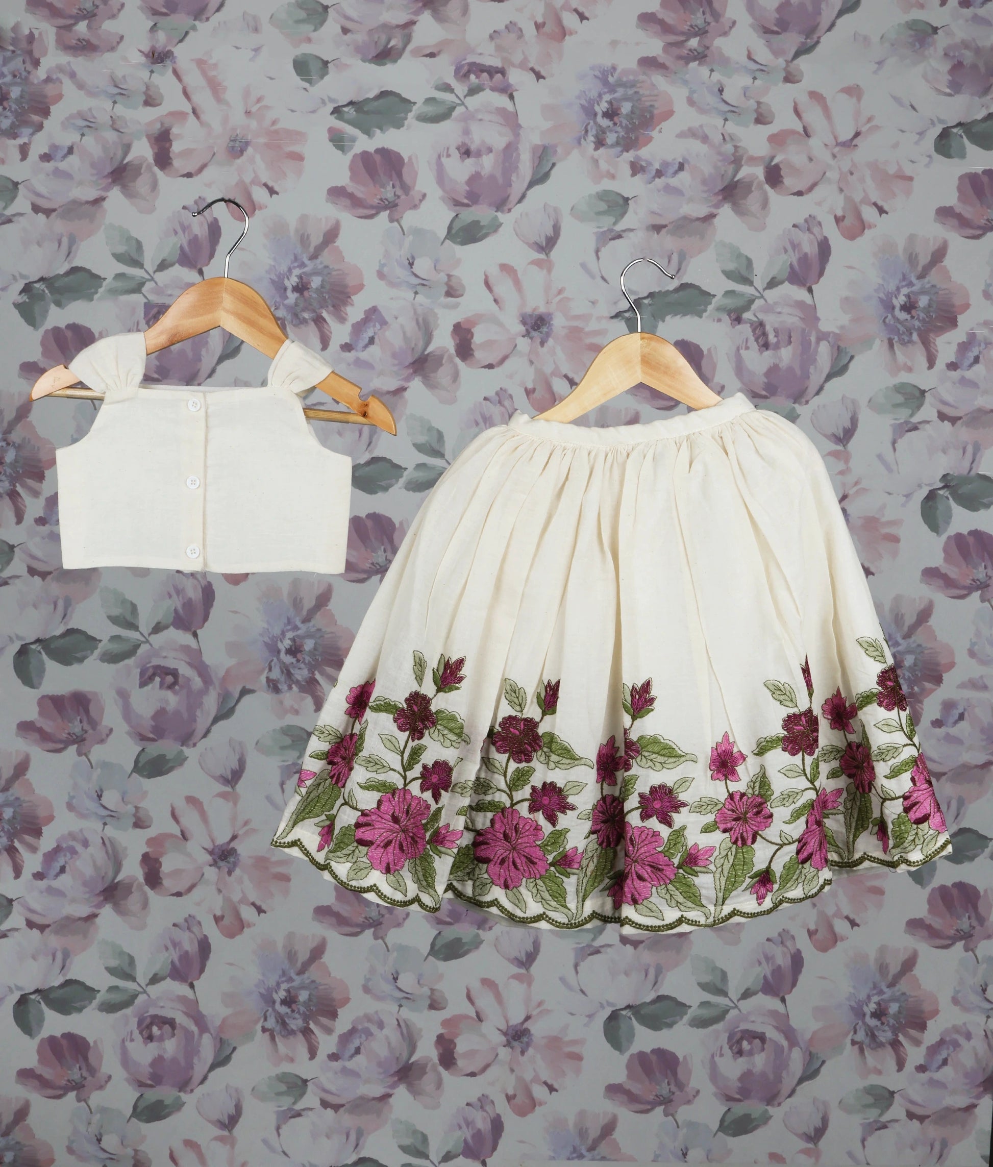 Back view of an skirt set on hangers against a floral wallpaper background.