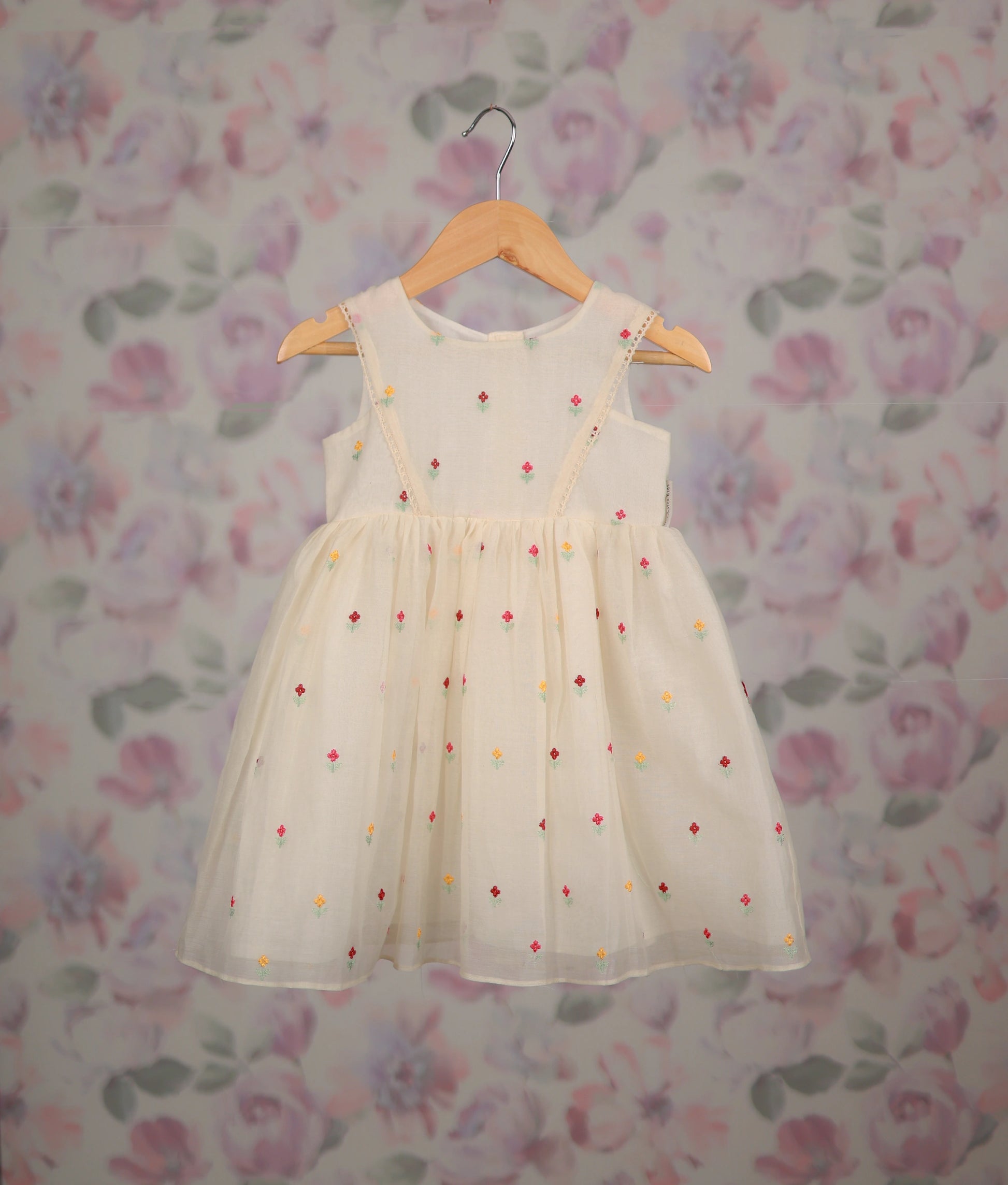 Off-white frock with colorful floral embroidery against a floral background.