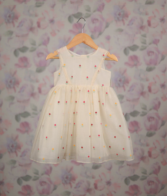 Off-white frock with colorful floral embroidery against a floral background.