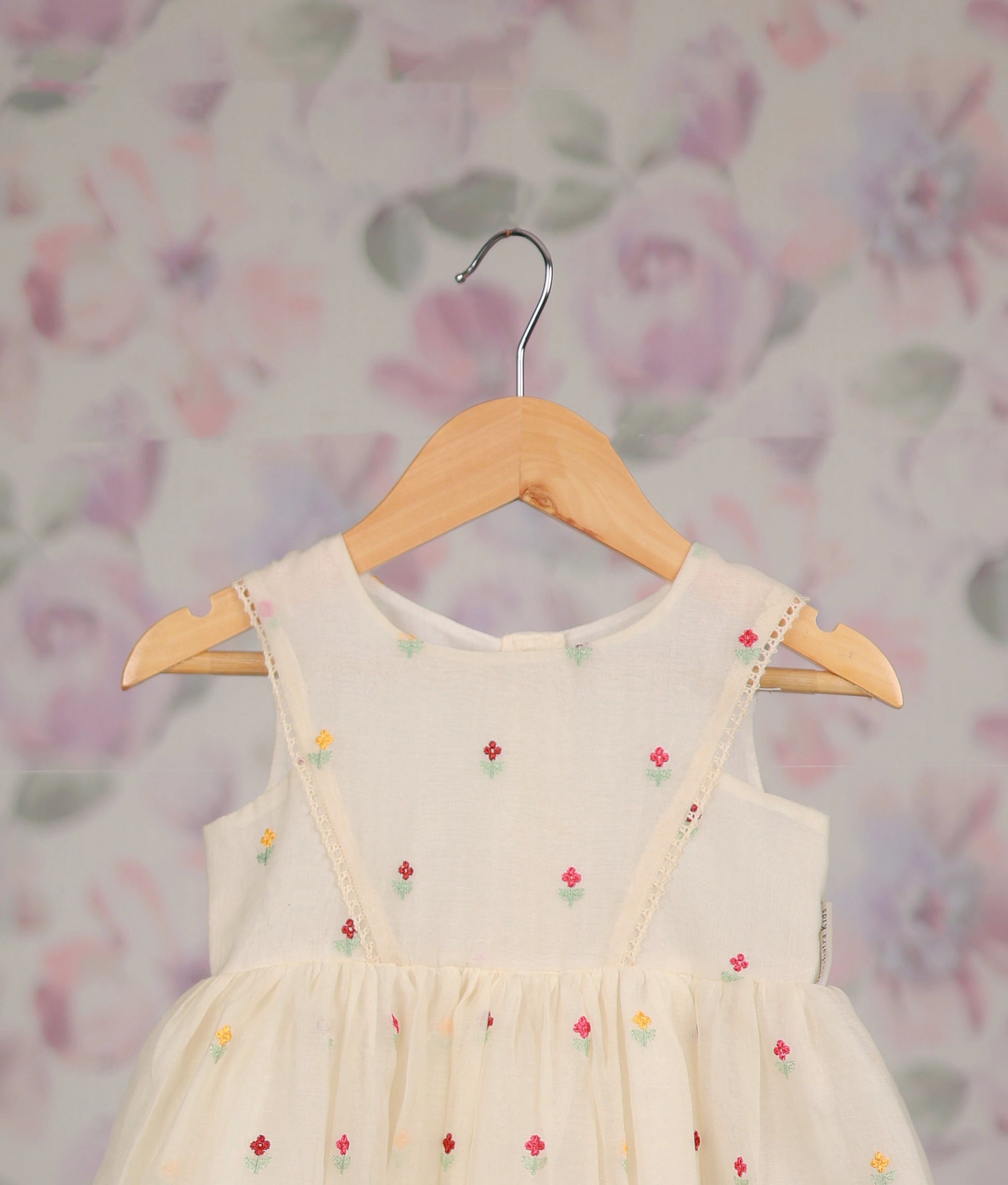 Close view of an off-white frock with colorful floral embroidery against a floral background.