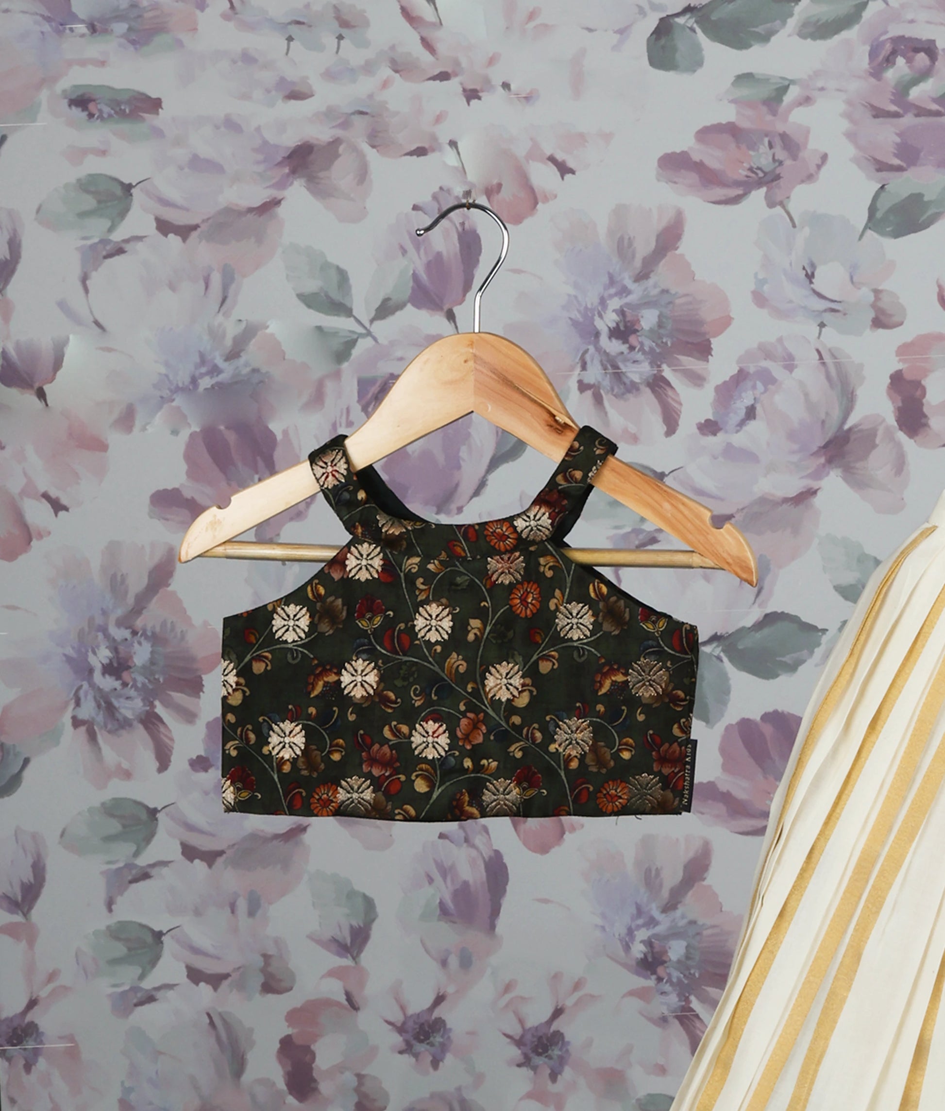 Close view of a floral green crop top and golden striped pleated skirt set against a floral background.