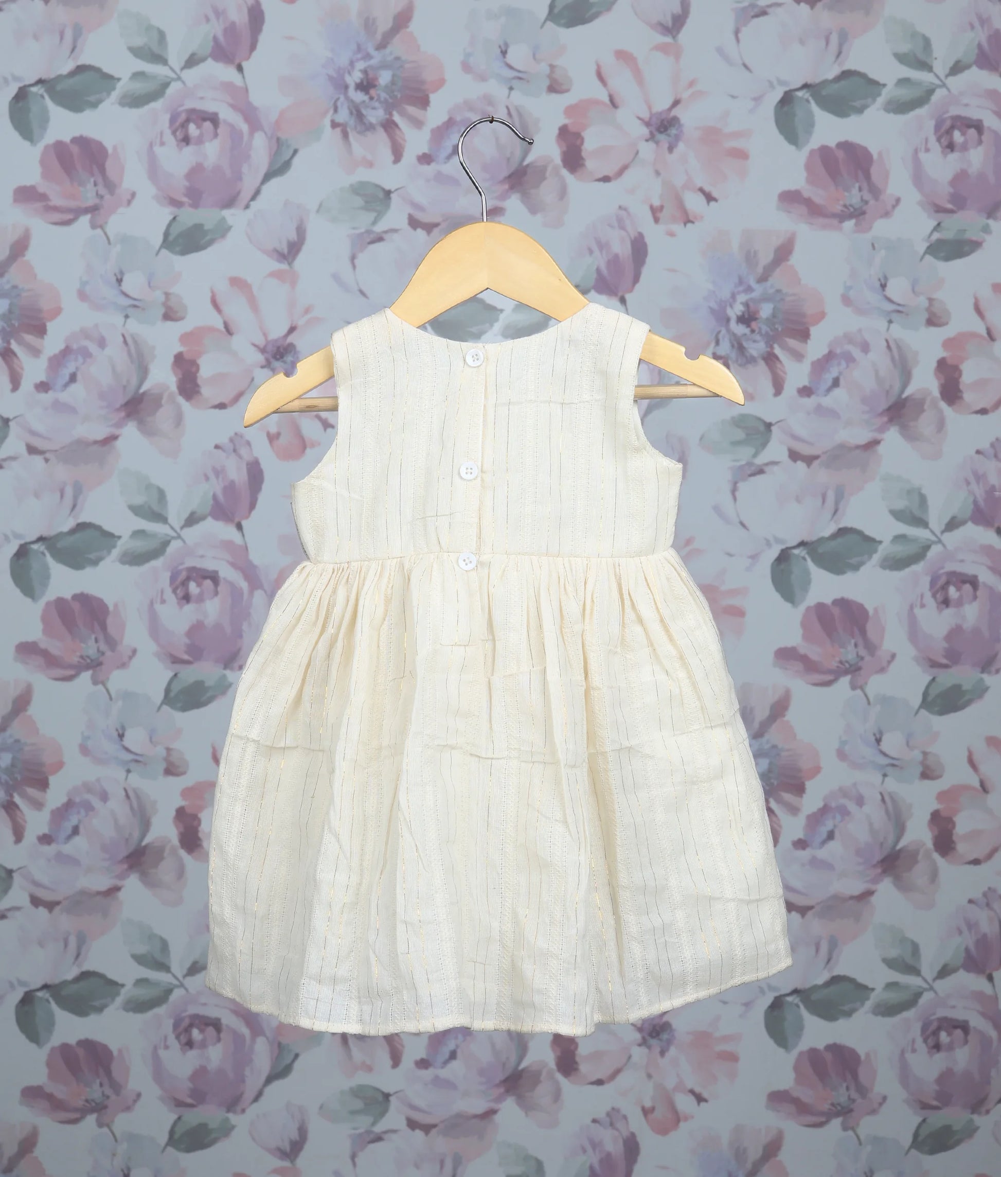 Back view of an off-white sleeveless baby dress with yellow floral embroidery and pleated frock on hangers.