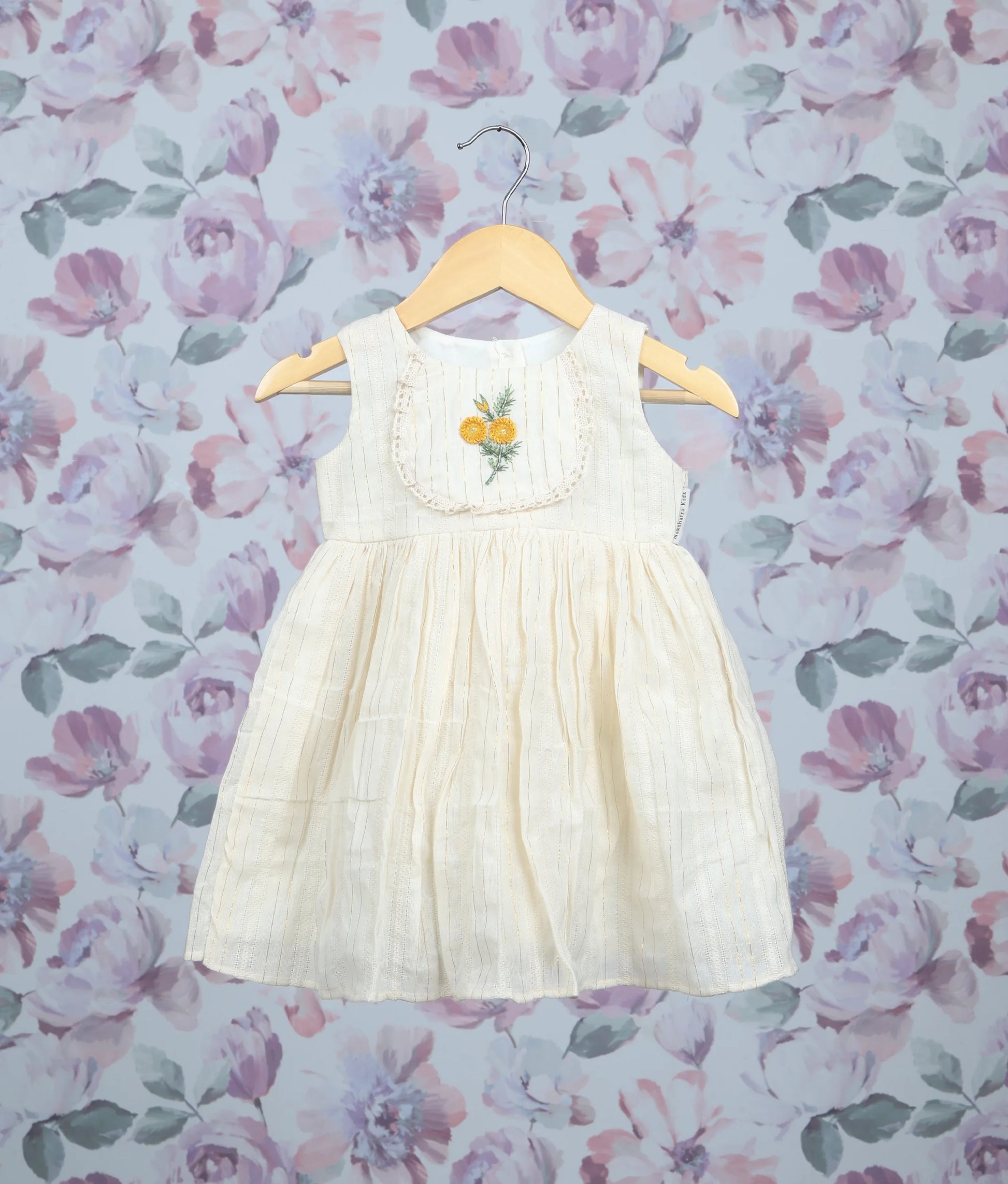 Off-white sleeveless baby dress with yellow floral embroidery and pleated frock on hangers.