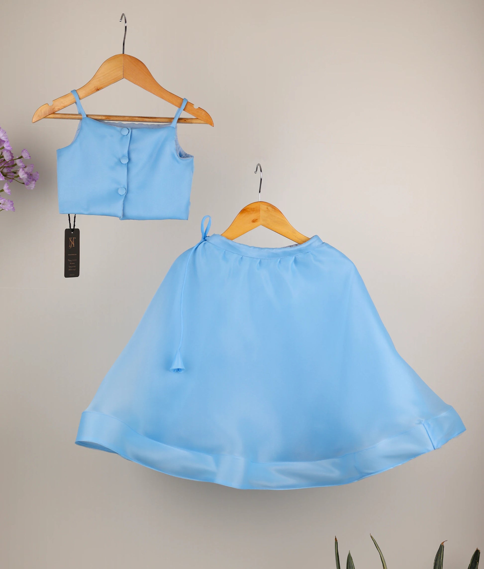 Back view of a sky blue girls' outfit with a handworked floral short top and skirt on wooden hangers.