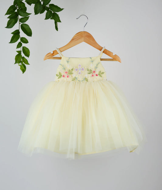 Front view of a pastel yellow tulle net floral handworked birthday frock.