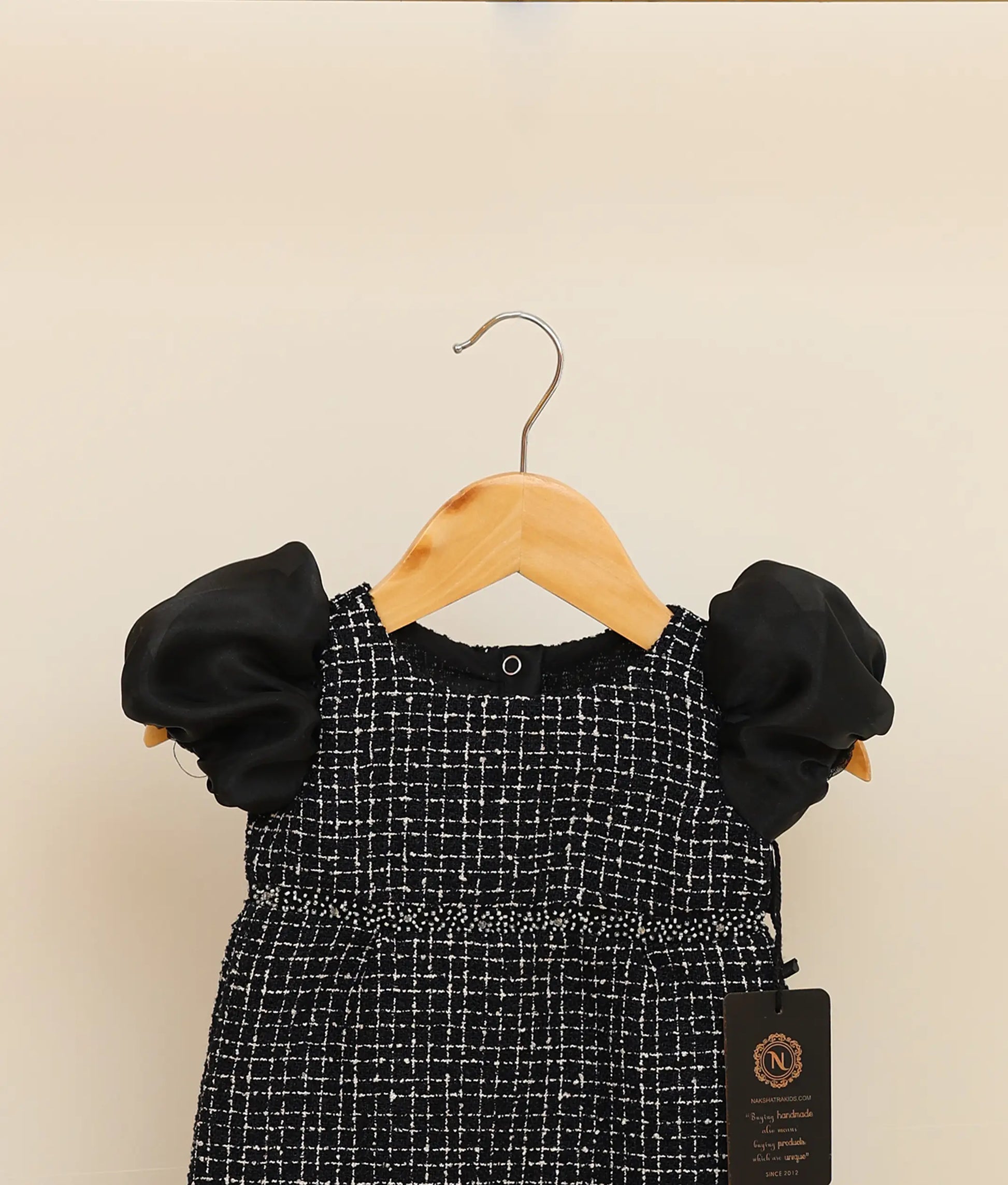 Close view of a black tweed handworked fish-cut frock against plain background