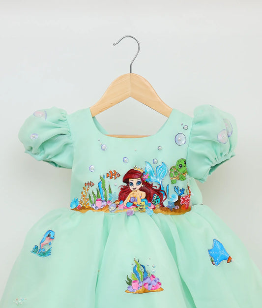 Close view of sea green plain organza painting and handworked mermaid-themed birthday dress against plain background