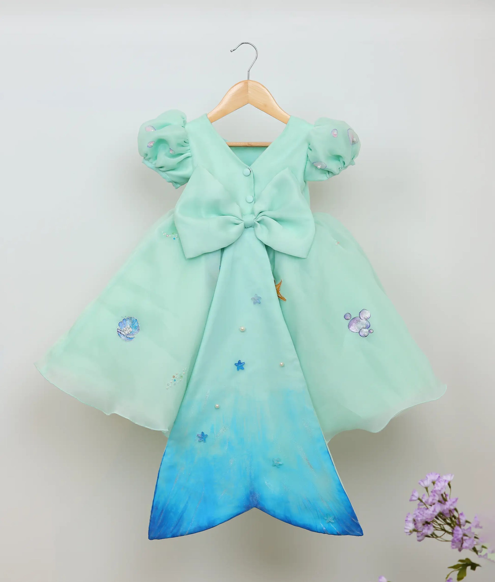 Back view of sea green plain organza painting and handworked mermaid-themed birthday dress against plain background