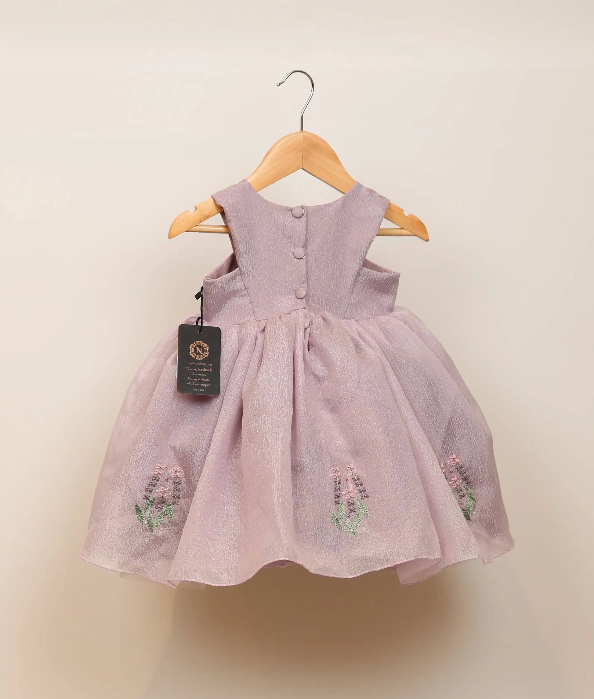 Back view of pastel lavender crush organza floral embroidery with handwork birthday frock against plain background 