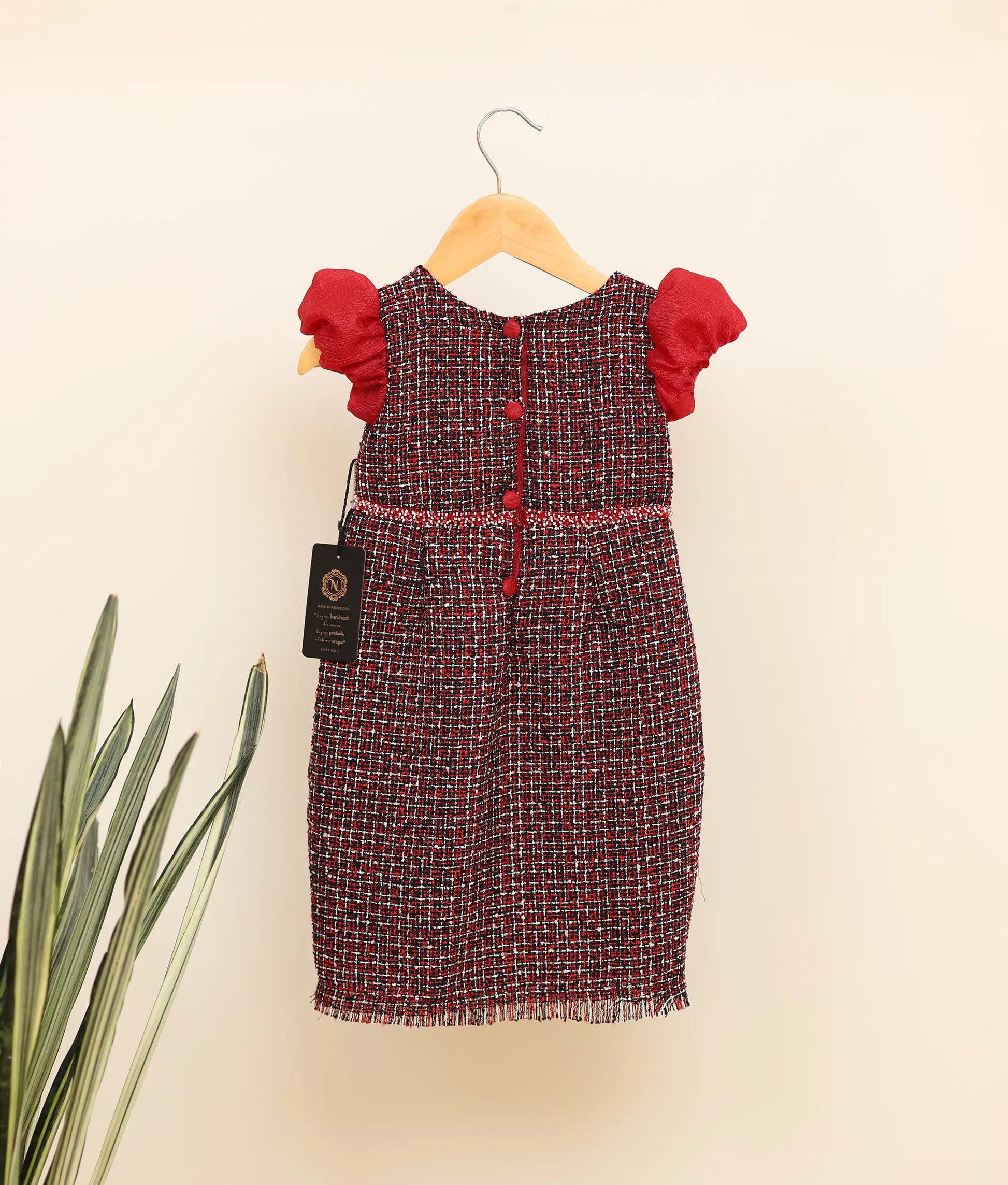 Back view of black handworked tweed handworked fish-cut frock against plain background 