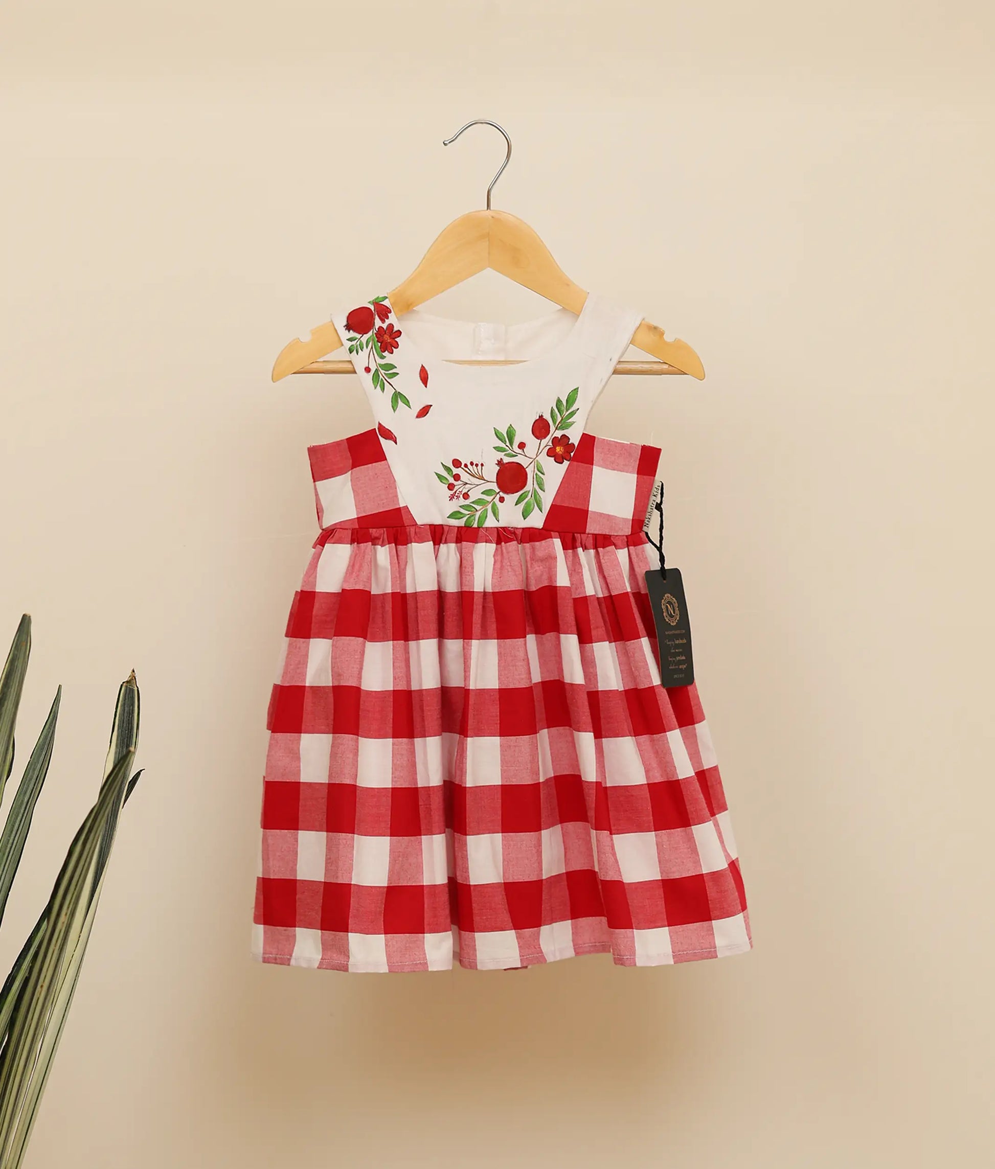 Front view of red check cotton floral painting Christmas frock against plain background.