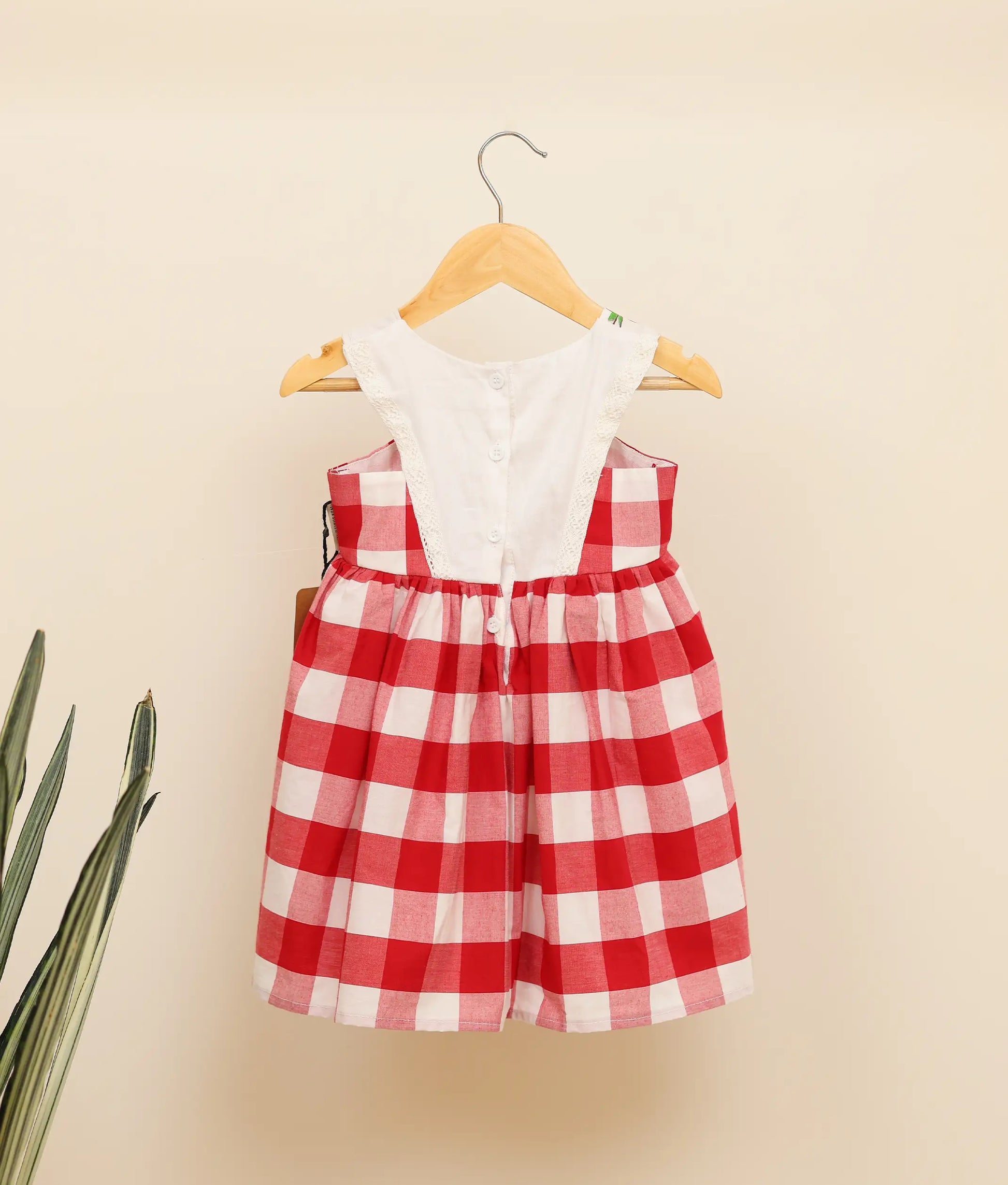 Back view of red check cotton floral painting Christmas frock against plain background